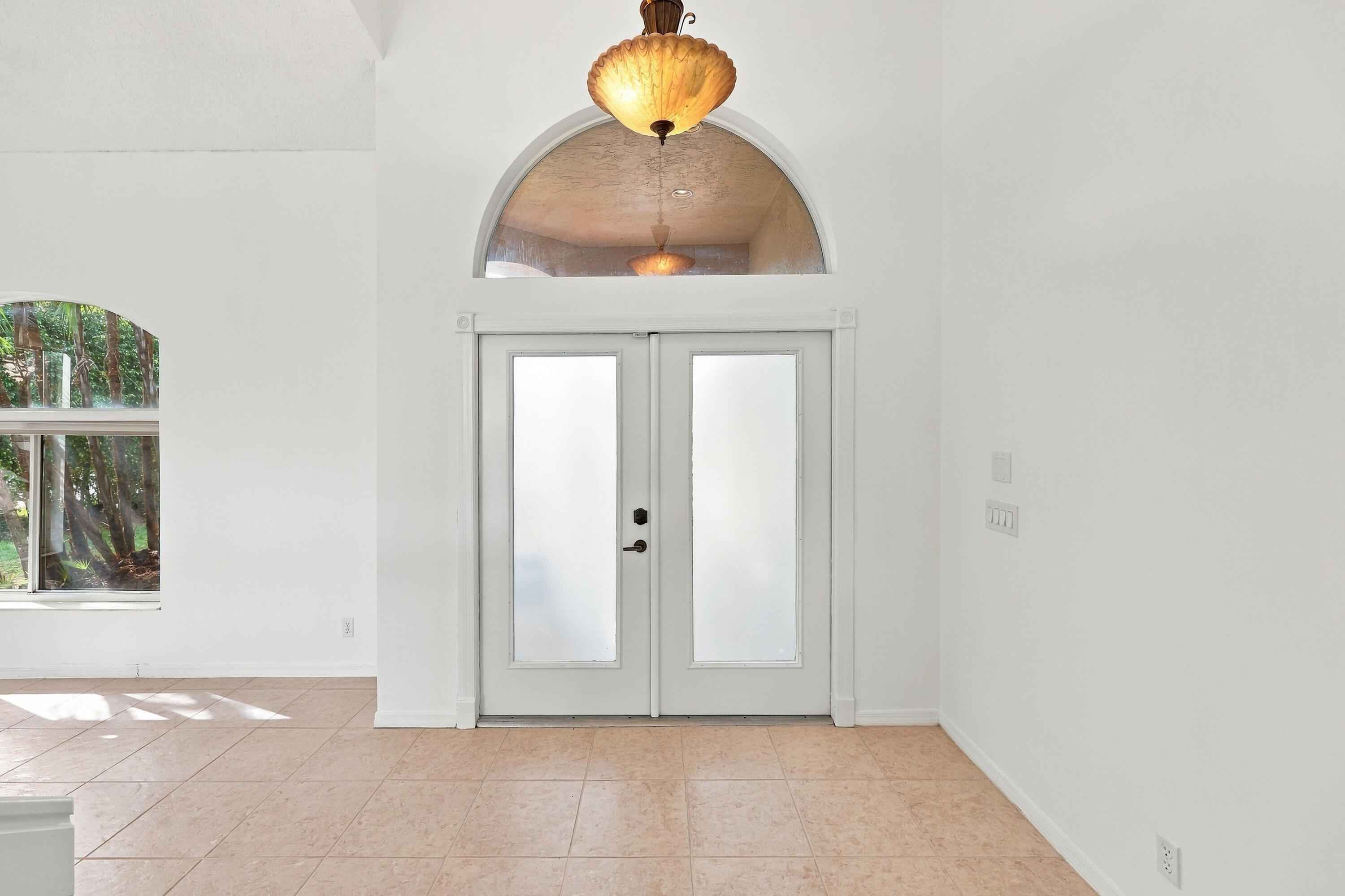 A welcoming entrance featuring elegant double doors, a decorative arched transom window, soaring ceilings, and an abundance of natural light. A welcoming entrance featuring elegant double doors, a decorative arched transom window, soaring ceilings, and an abundance of natural light.