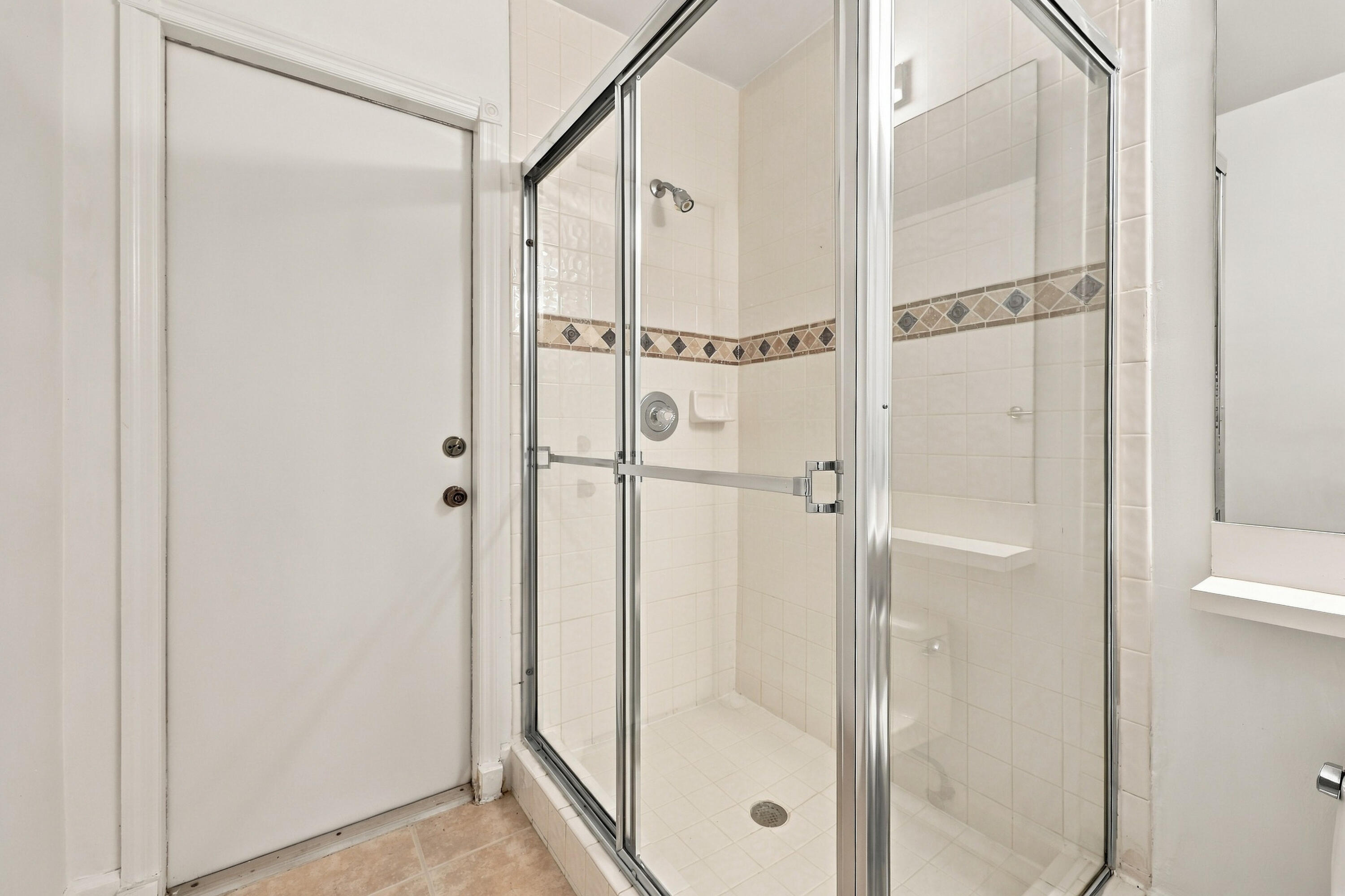 A convenient main-level guest bathroom featuring a glass-enclosed walk-in shower with decorative tile accents and neutral finishes.