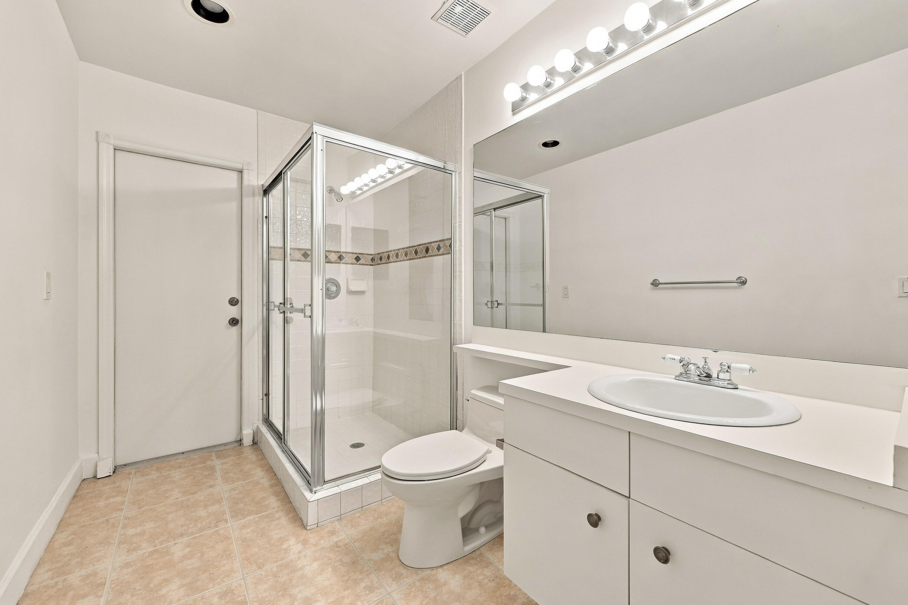 This well-appointed full bathroom features a spacious vanity, large mirror, glass-enclosed shower, and convenient access from the main living areas and guest bedroom.