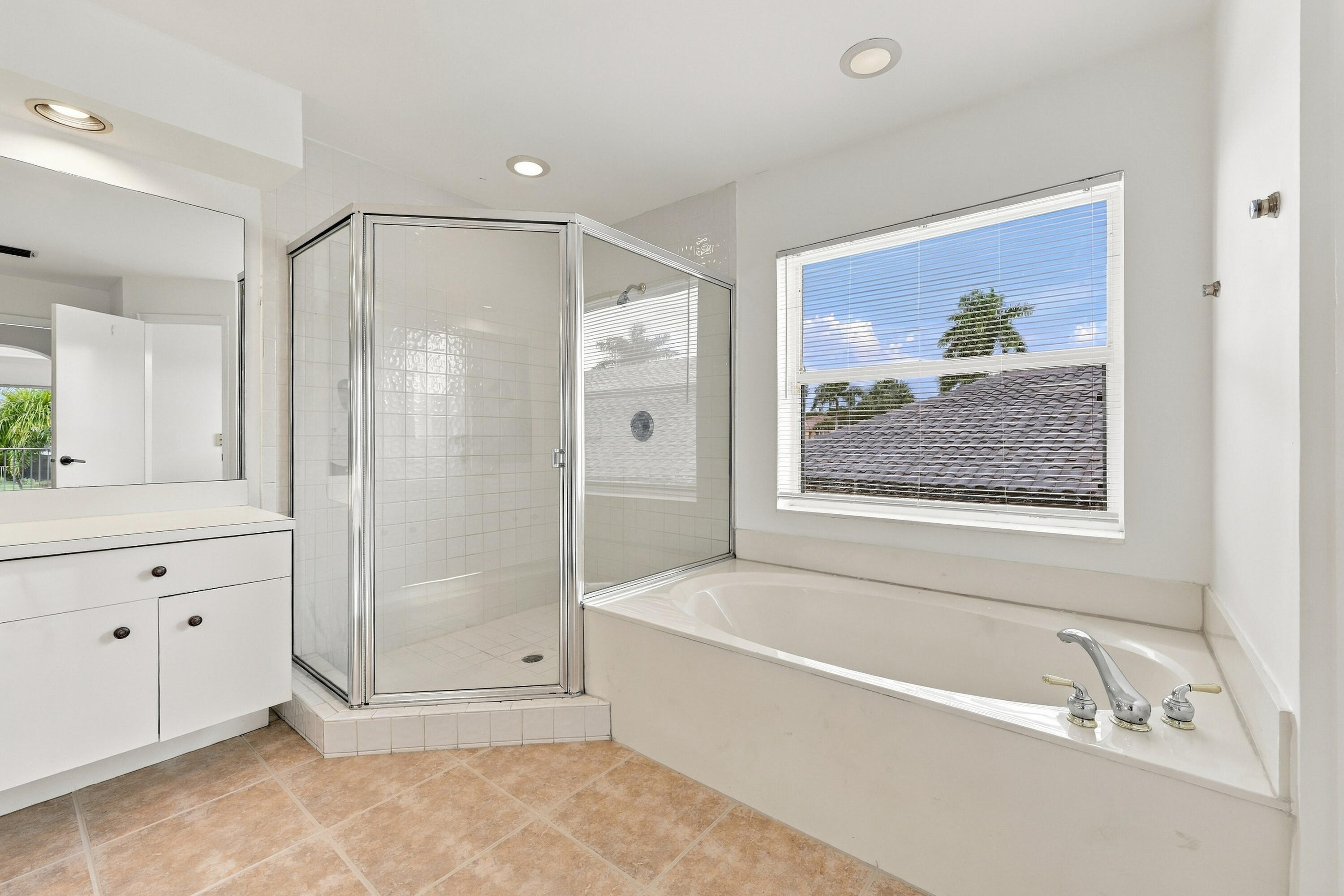 A spacious primary bathroom featuring a relaxing soaking tub beneath a large window, a glass-enclosed shower, and neutral finishes that create an inviting atmosphere.