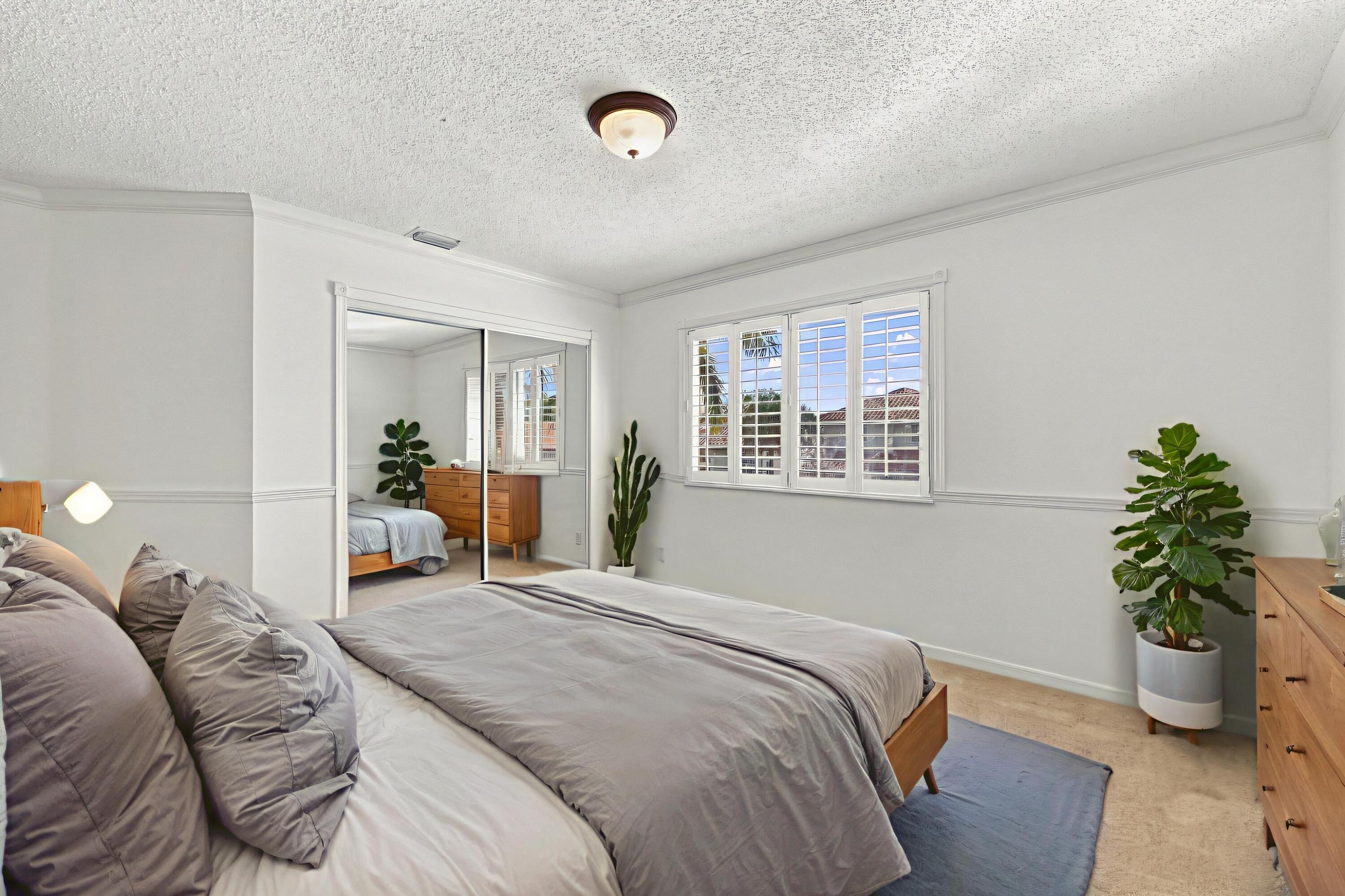 This generously sized third bedroom features plush carpeting, plantation shutters, mirrored closet doors, and decorative wall molding that adds character.