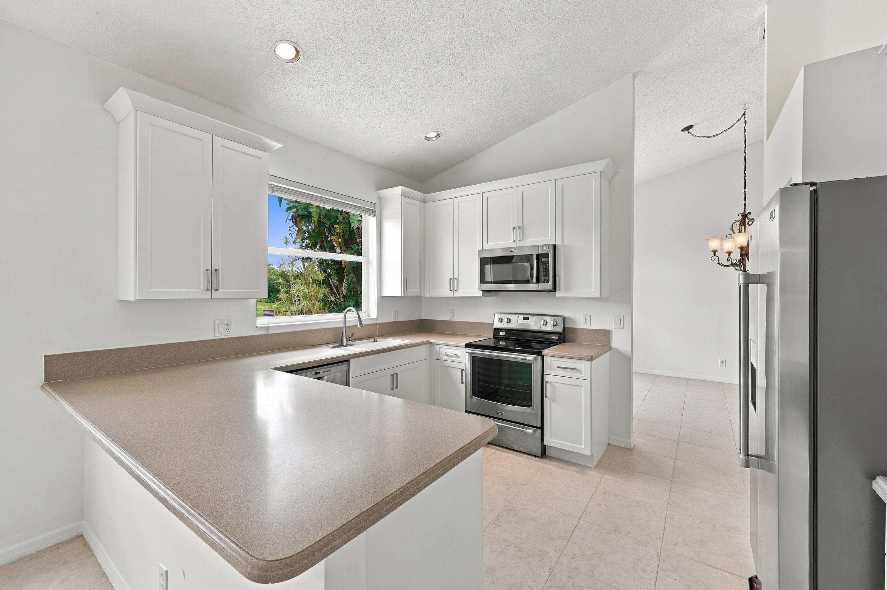 A thoughtfully arranged kitchen offering extensive counter space, white cabinetry, stainless steel appliances, and convenient access to the adjoining breakfast area.