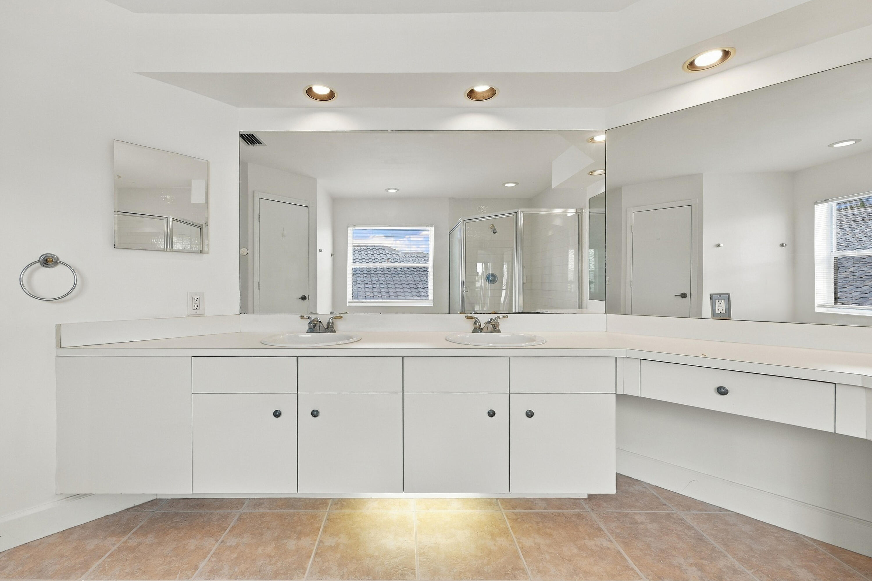 An impressive primary bathroom featuring an extended vanity with abundant cabinetry, expansive mirrors, recessed lighting, and a dedicated makeup station.