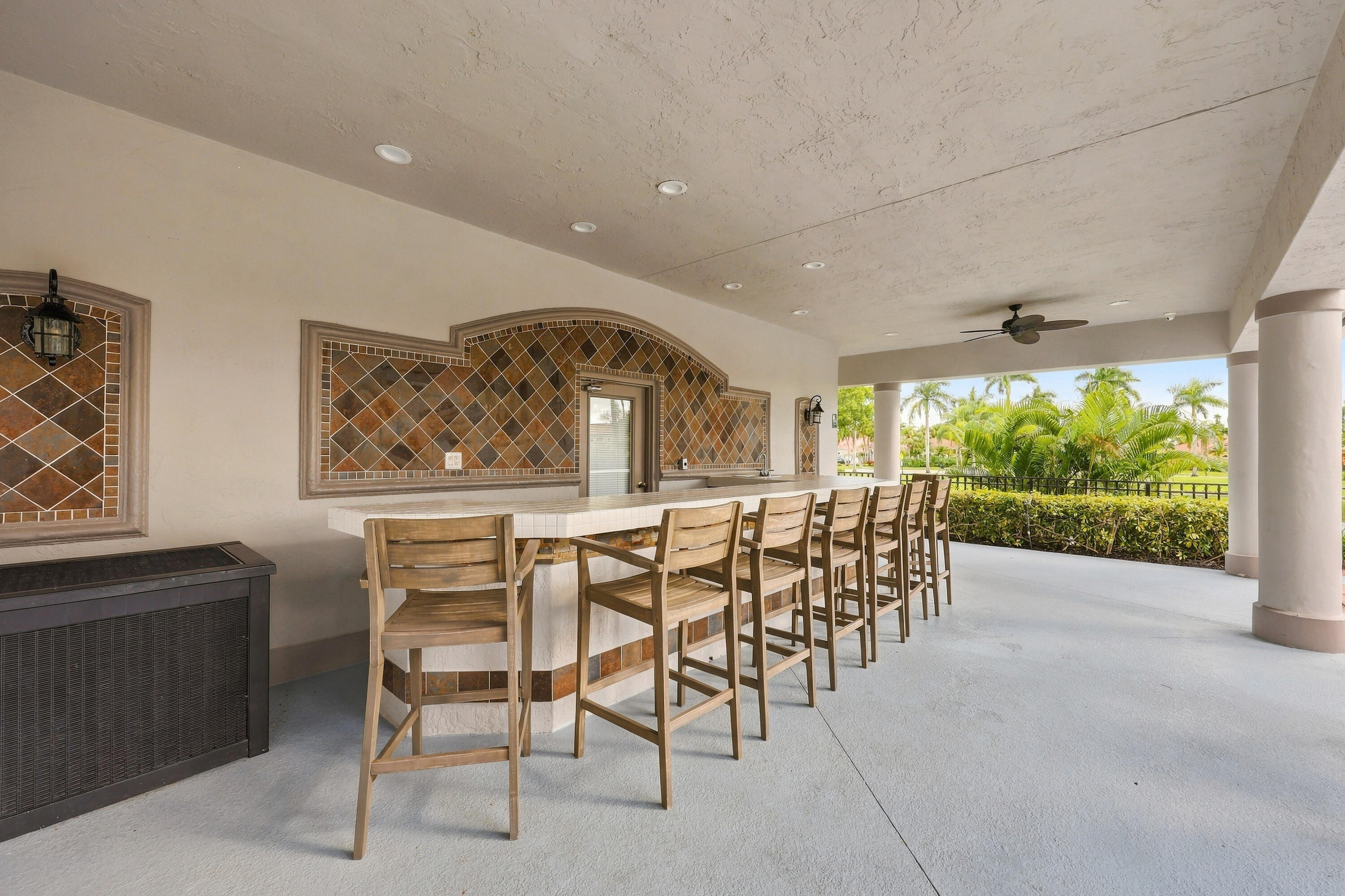 An inviting covered outdoor entertaining area featuring bar-style seating and ceiling fans, perfect for socializing and enjoying the beautiful South Florida weather.
