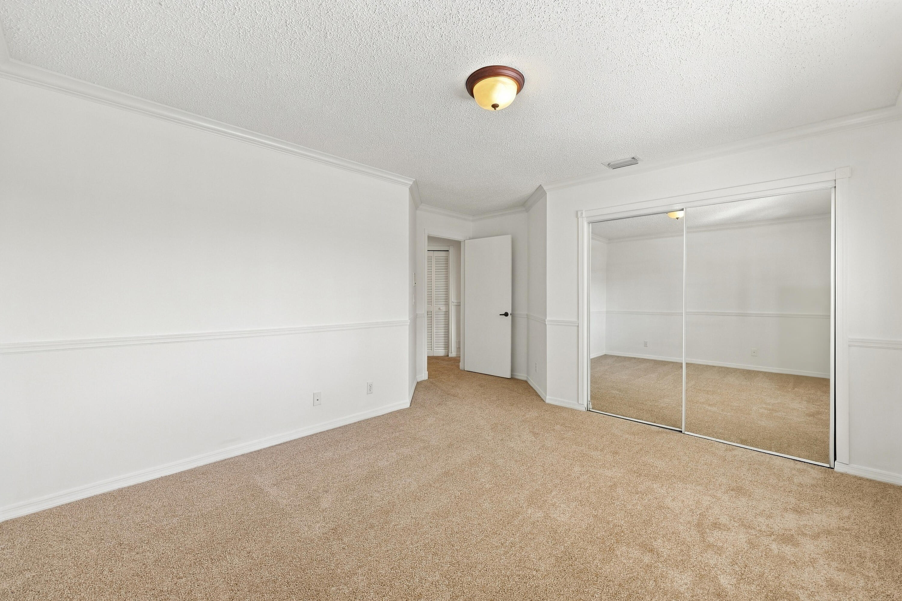 An inviting third bedroom offering a large mirrored closet, neutral finishes, and ample space for comfortable living.