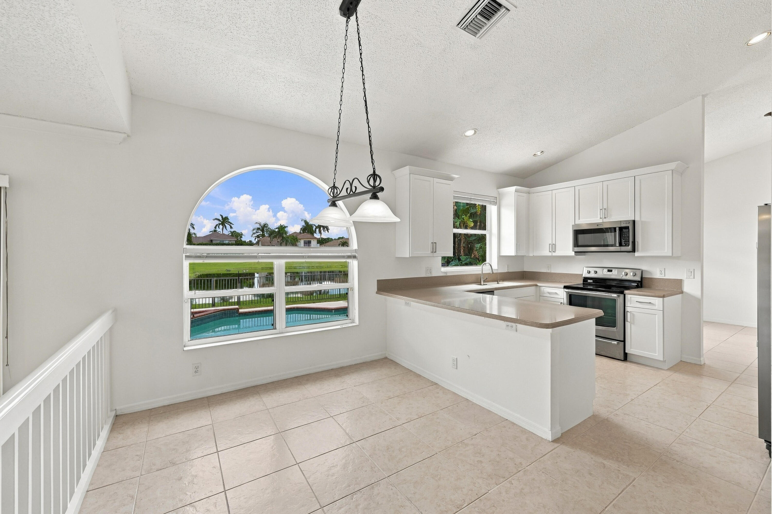 Enjoy picturesque views of the surrounding greenery from the charming breakfast nook, complete with an oversized arched window, vaulted ceilings, and decorative lighting.