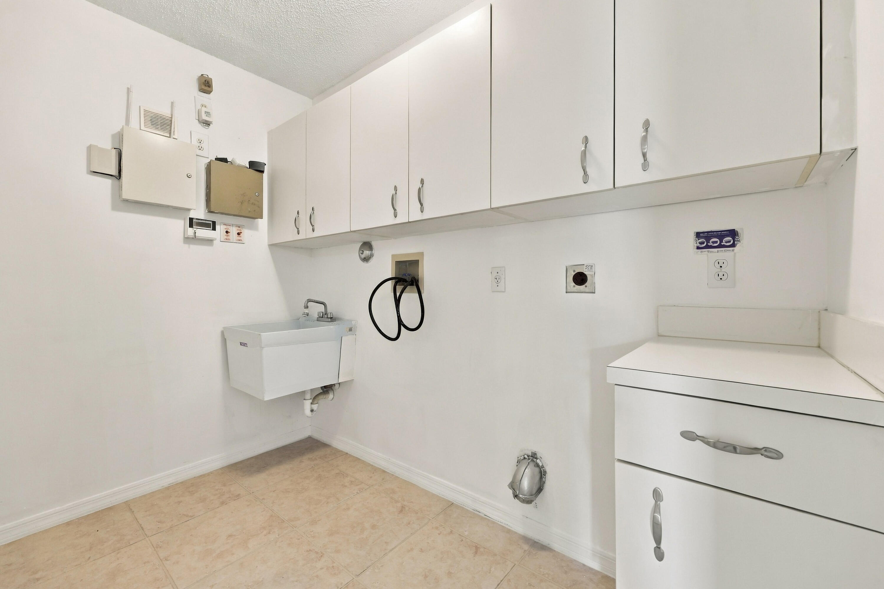 Conveniently located on the first floor, this dedicated laundry room features abundant overhead cabinetry, a utility sink, neutral tile flooring, and plenty of space for laundry appliances and household storage.