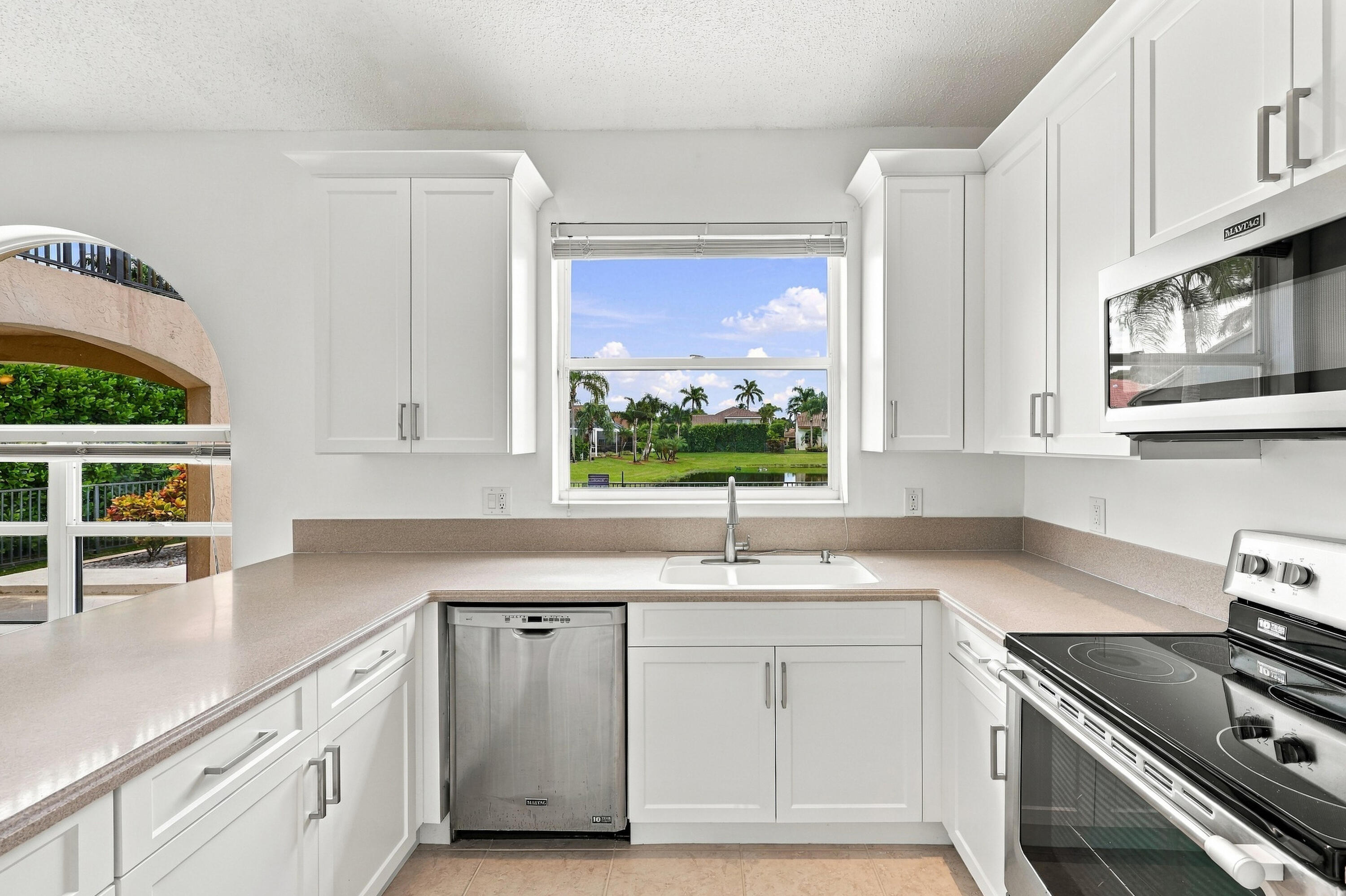 White cabinetry, stainless steel appliances, and generous counter space complement a large kitchen window overlooking the beautifully landscaped outdoor surroundings.