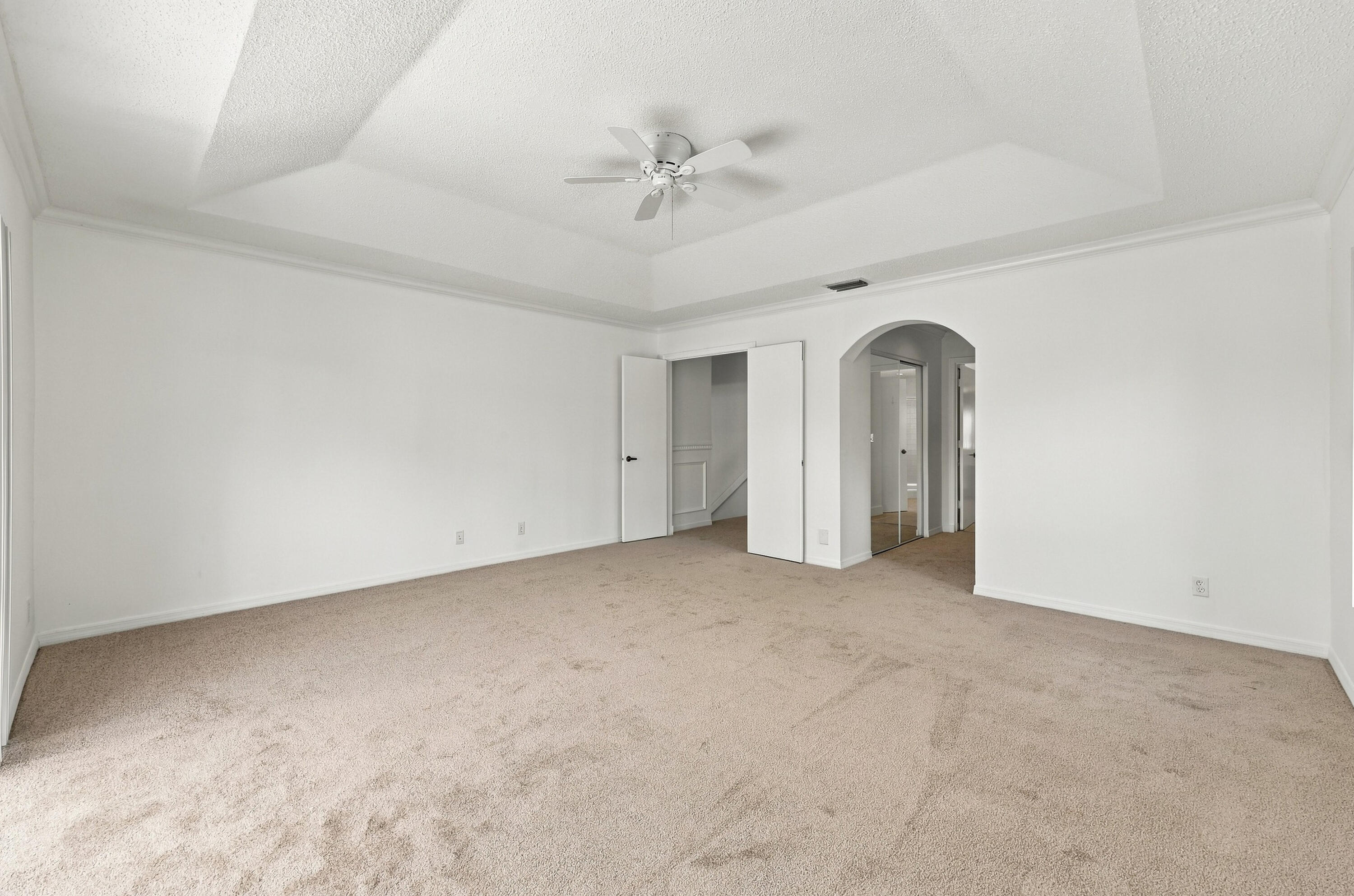 This generously sized primary suite offers an elegant tray ceiling, plush carpeting, and an expansive layout with plenty of room to create your own personal retreat.