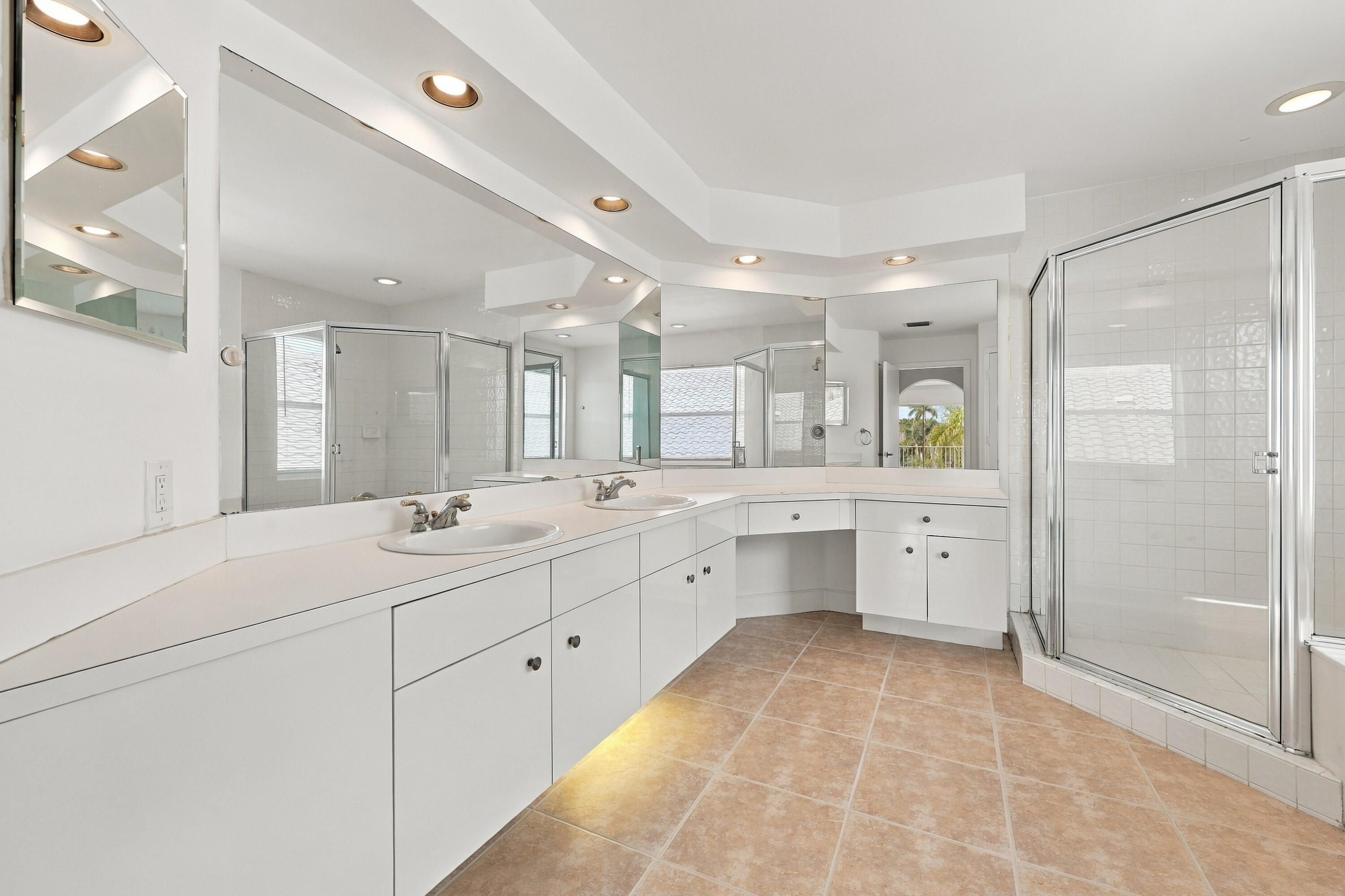 Generous counter space, dual sinks, extensive cabinetry, and a separate makeup vanity make this primary bathroom both functional and inviting.