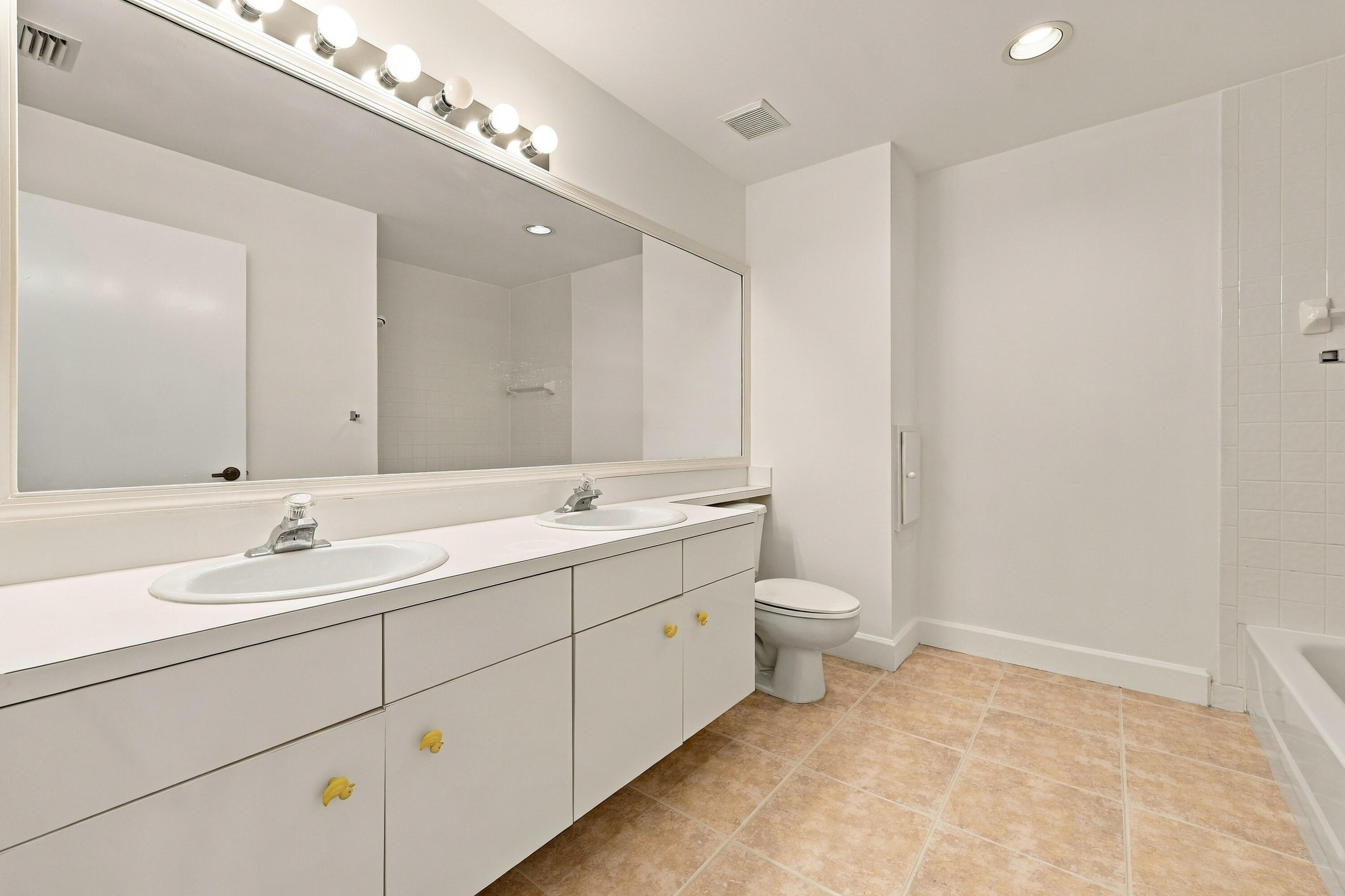 This well-appointed upstairs bathroom features an expansive dual-sink vanity, generous counter space, abundant cabinetry, and a large mirror with overhead lighting.
