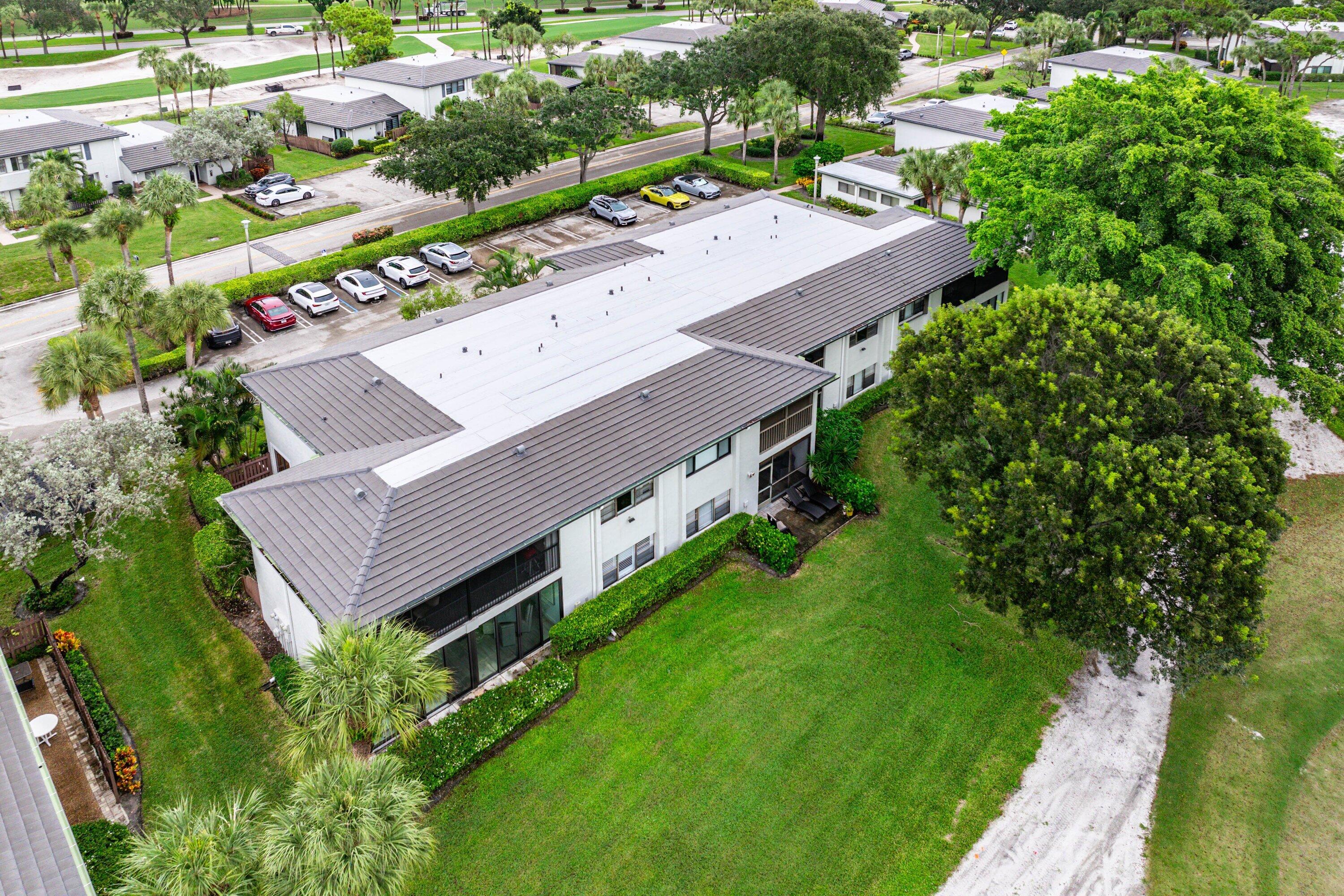Aerial perspective of a multi-unit building featuring a metal roof, screen-enclosed balconies, and landscaped green space
