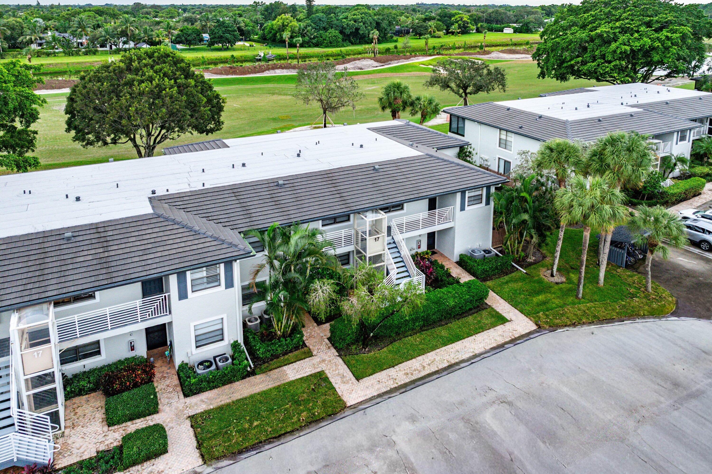 Multi-story residential buildings featuring low-slope tile roofing, exterior staircases with white metal railings, paver walkways, and manicured tropical landscaping