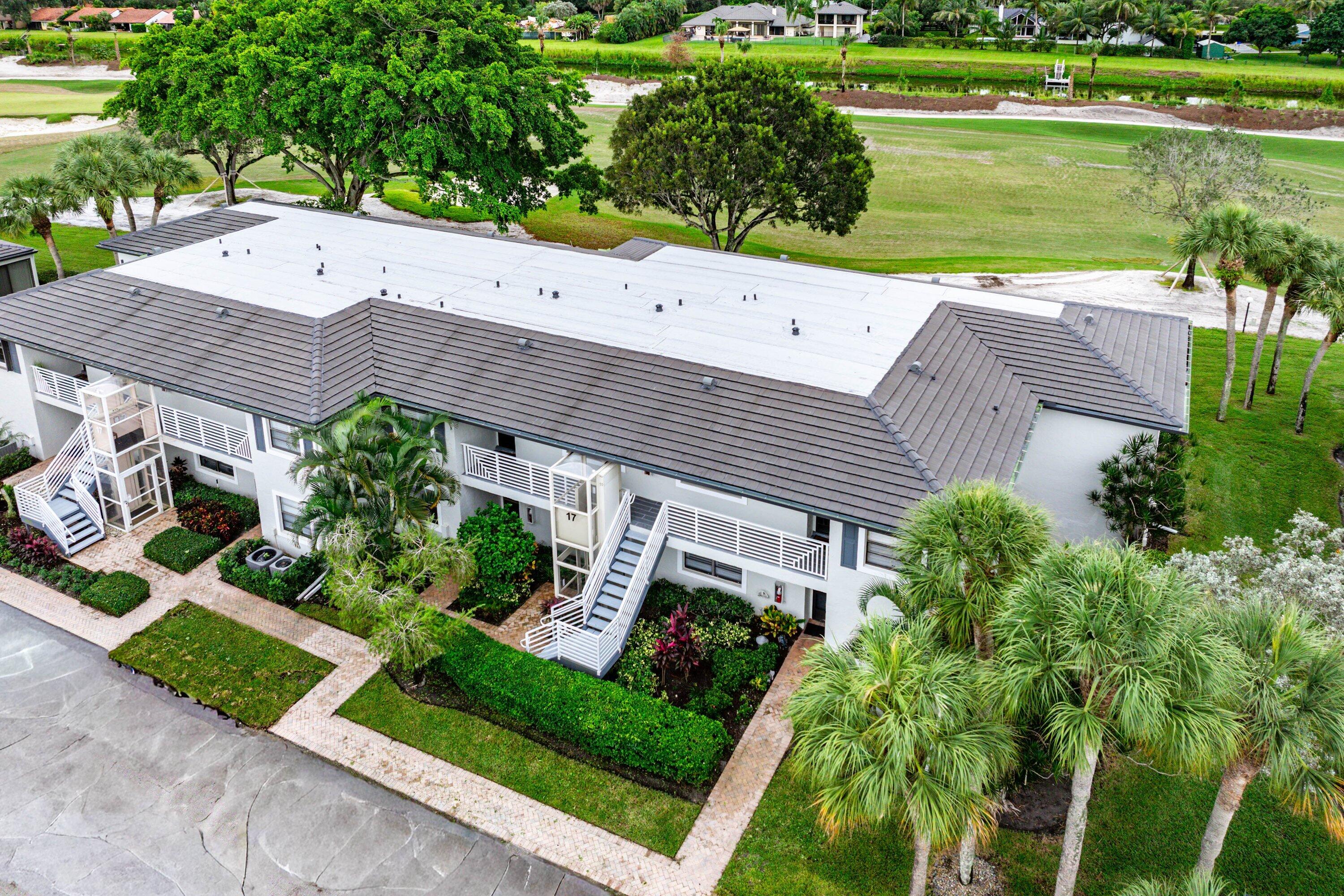 Multi-level building featuring a pitched tile roof, exterior staircases, railed balconies, and extensive perimeter landscaping with mature palm trees