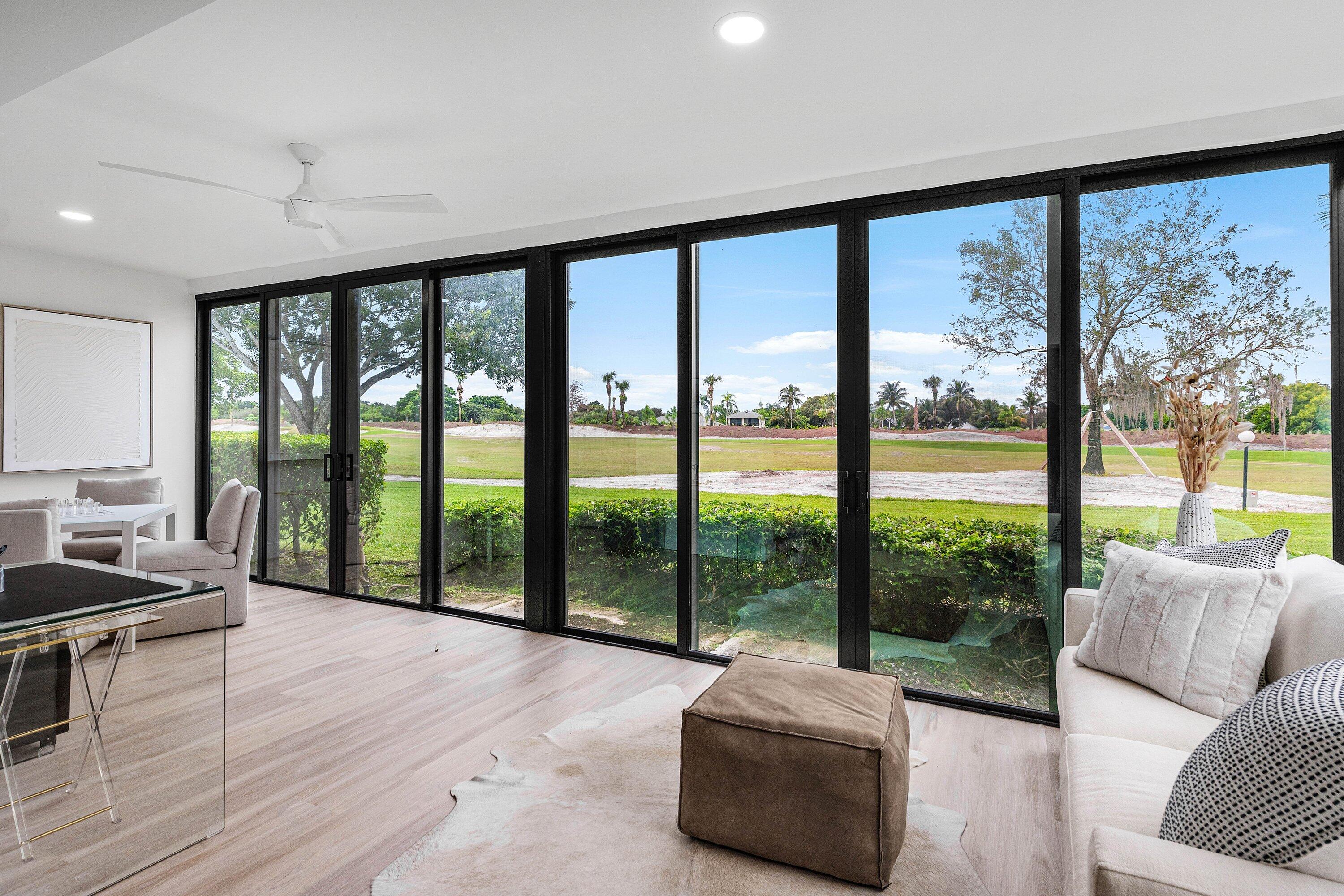 Floor-to-ceiling black-framed sliding glass doors, wood-finish flooring, recessed lighting, and a white ceiling fan