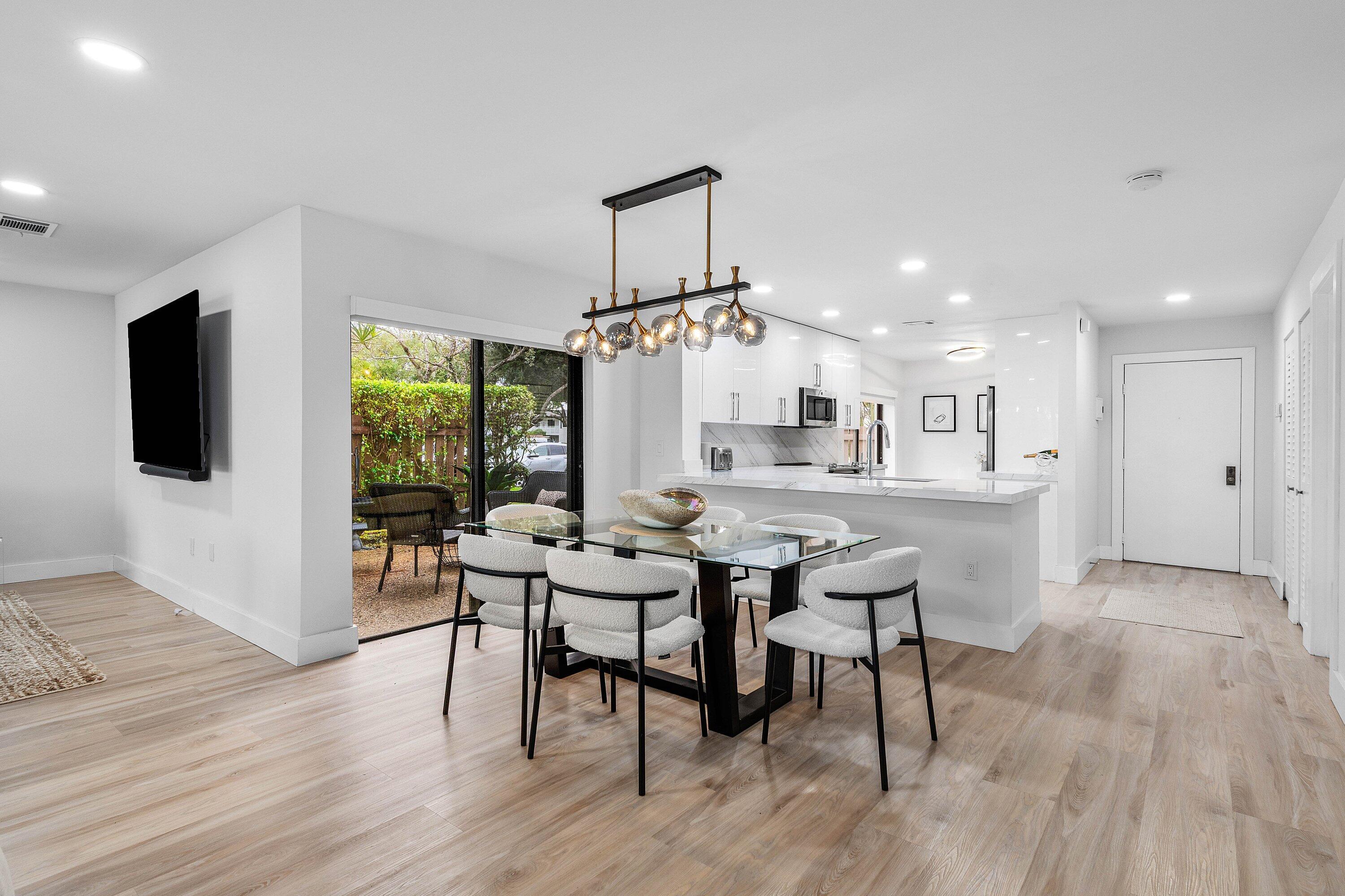 Open-concept interior featuring light wood-finish flooring, recessed lighting, a modern linear multi-bulb pendant fixture, white cabinetry, and sliding glass doors