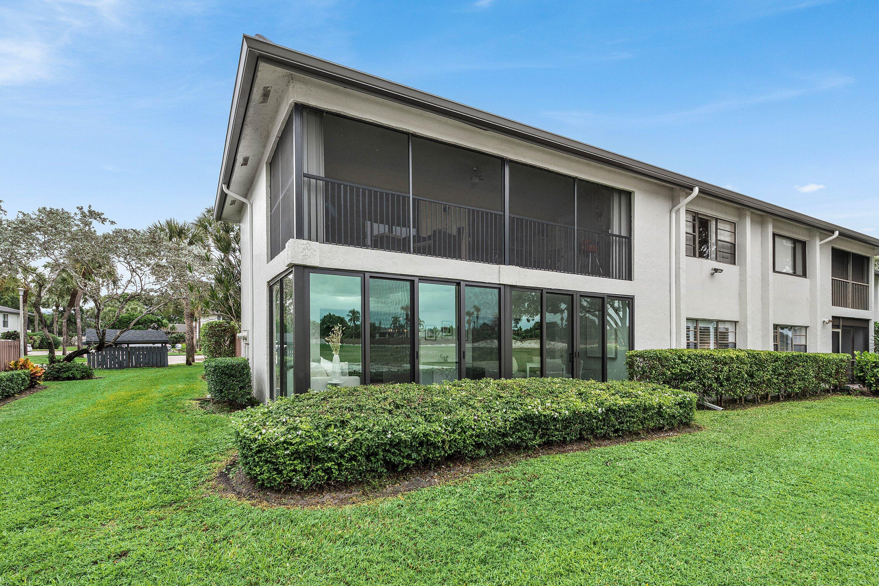 Two-story exterior featuring light-colored stucco finish, screened balcony with dark-toned metal railing, and floor-to-ceiling glass panel windows