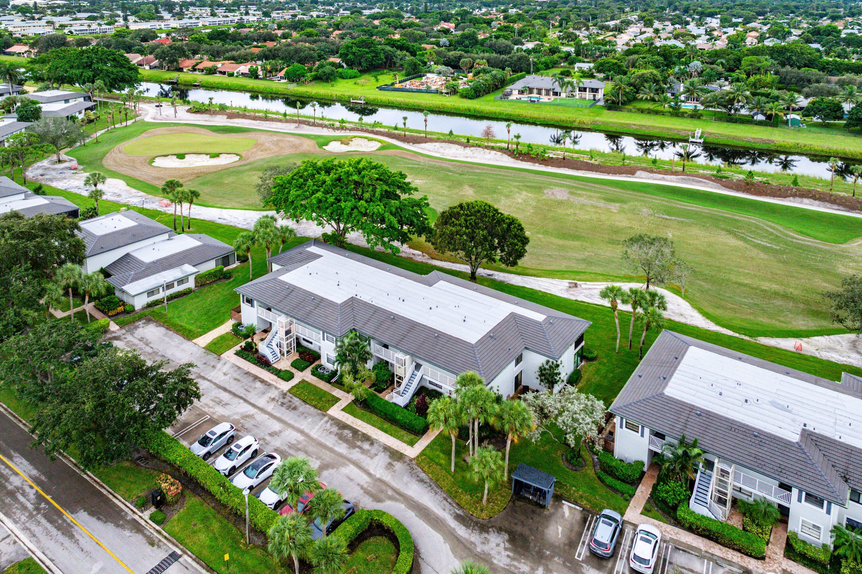 Aerial perspective of multi-family residences featuring hip-style rooflines, manicured landscaping, paved parking areas, and expansive water frontage bordering a golf course