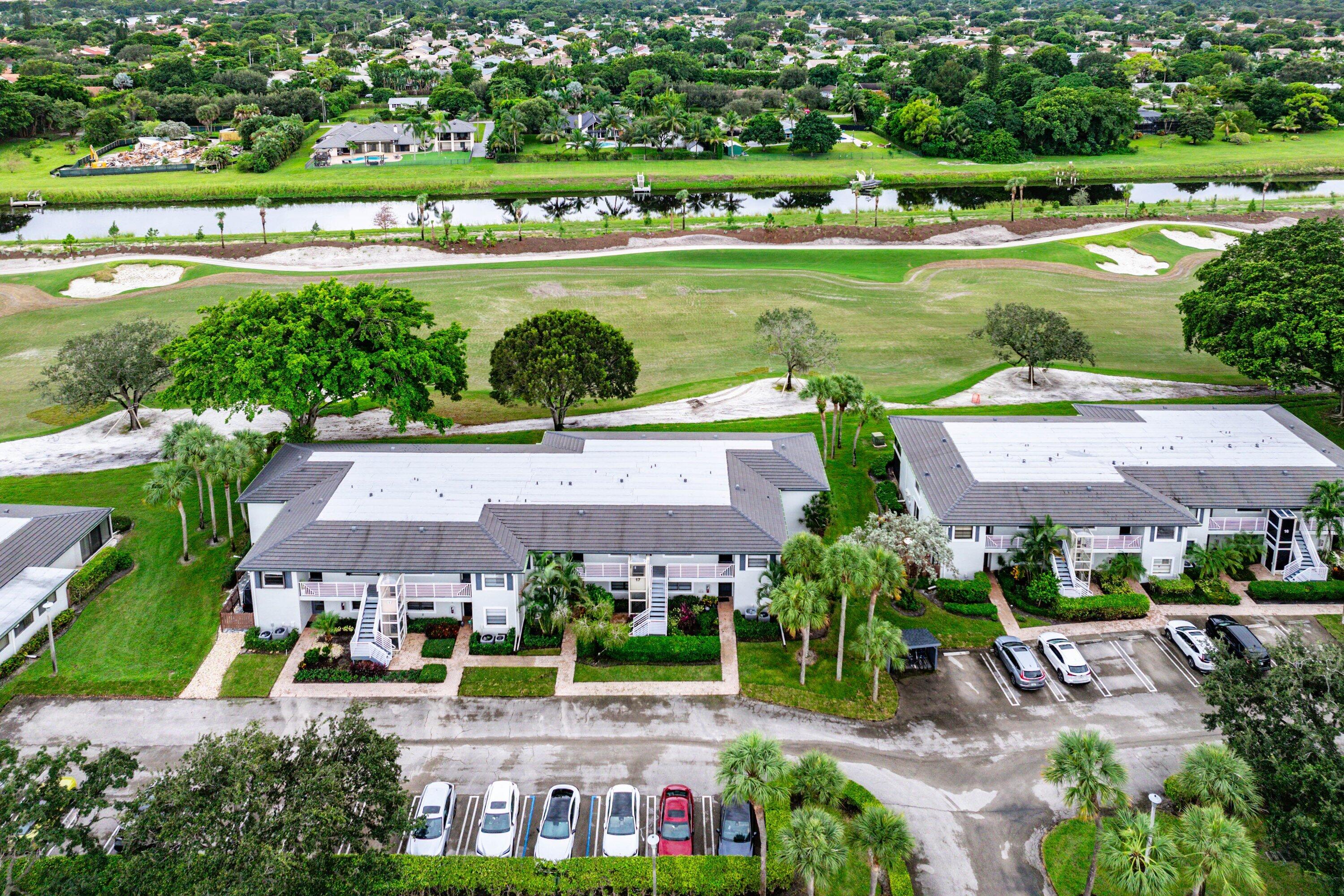 Aerial perspective featuring multi-unit structures with shingled roofs, integrated parking lots, and direct exposure to a golf course and waterway