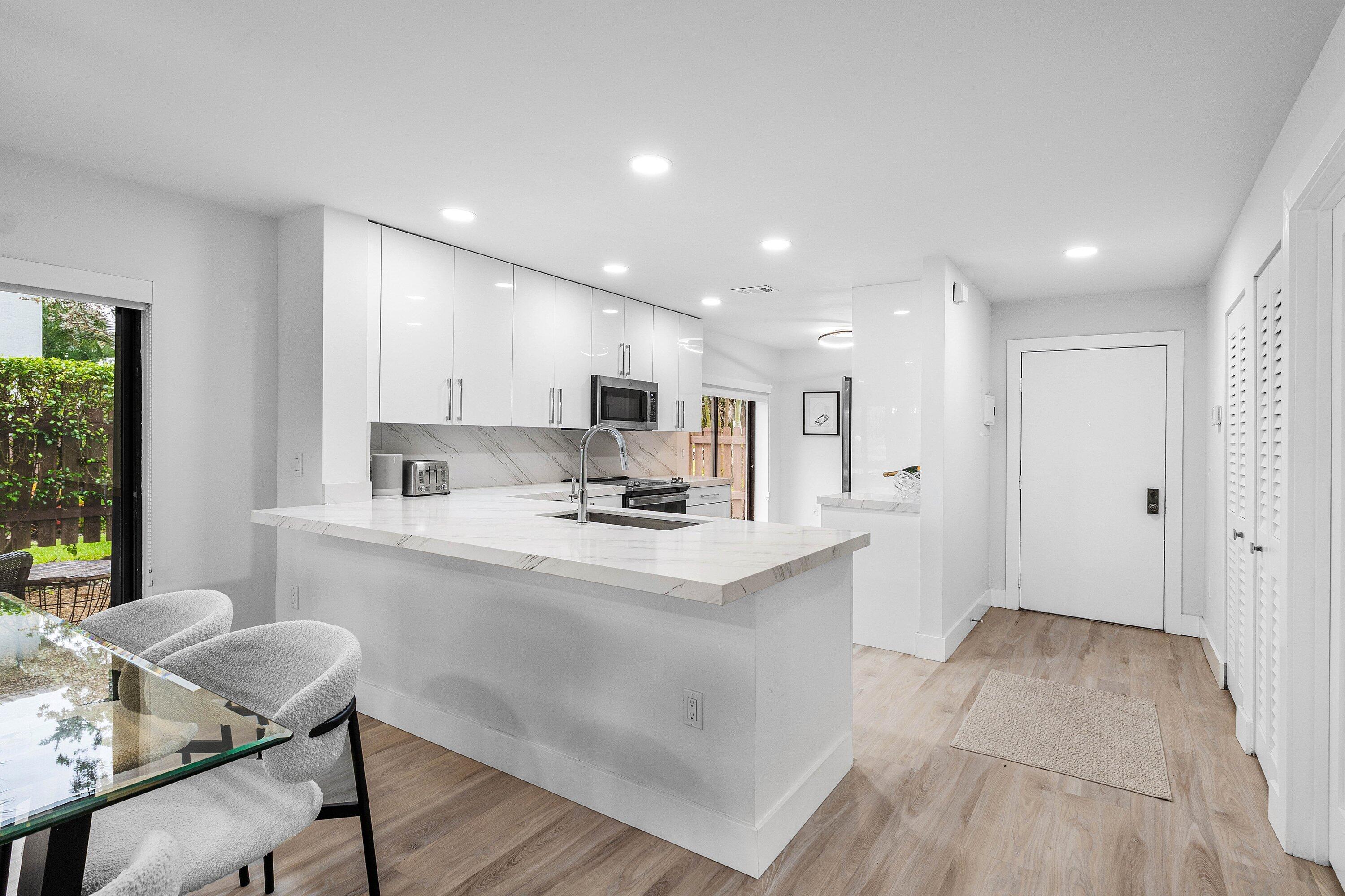 Kitchen featuring high-gloss white cabinetry, stone-finish countertops, undermount stainless steel sink, recessed lighting, and wood-finish flooring