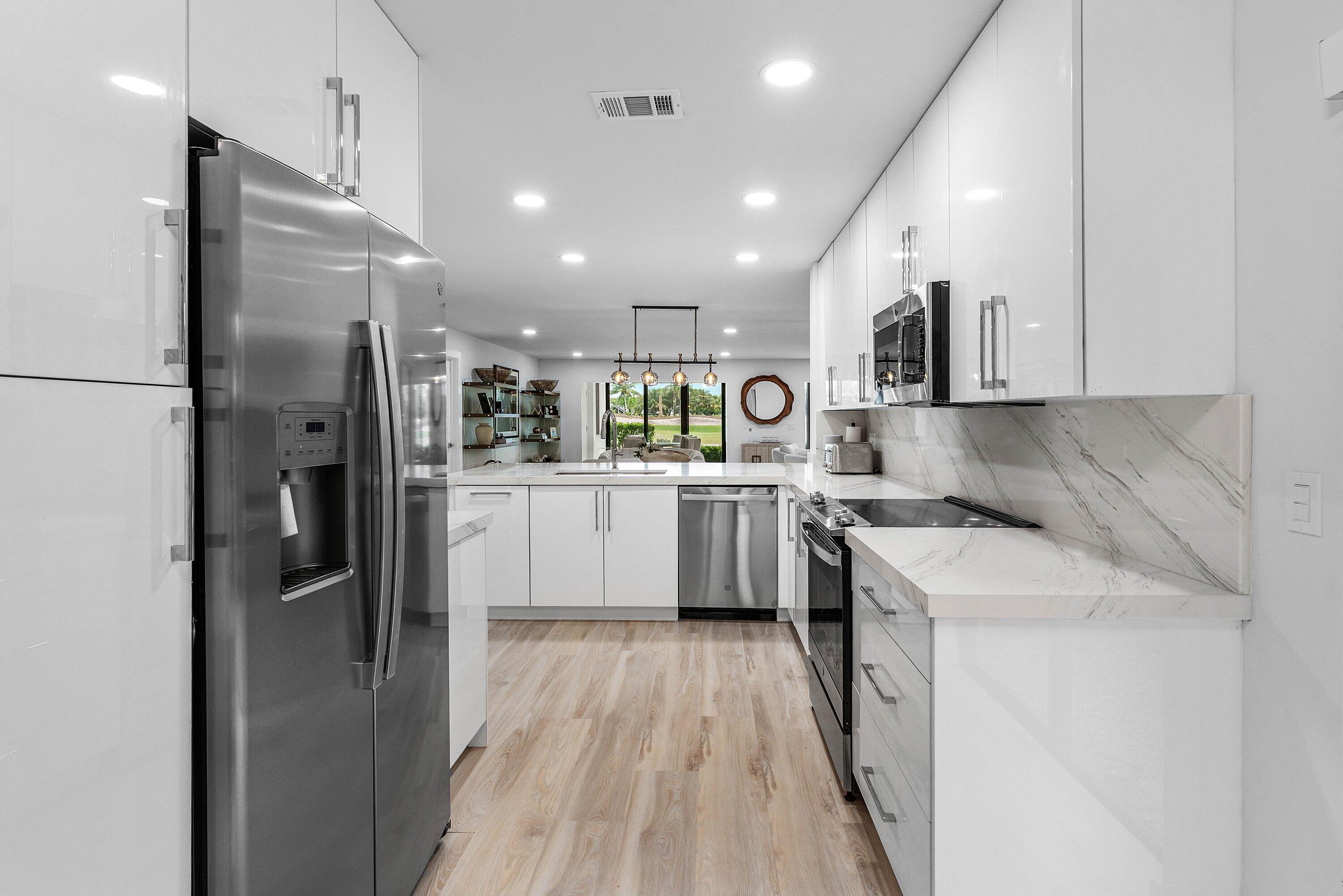 Modern kitchen featuring high-gloss white cabinetry, stainless steel appliances, stone-finish countertops with matching backsplash, and wood-finish flooring