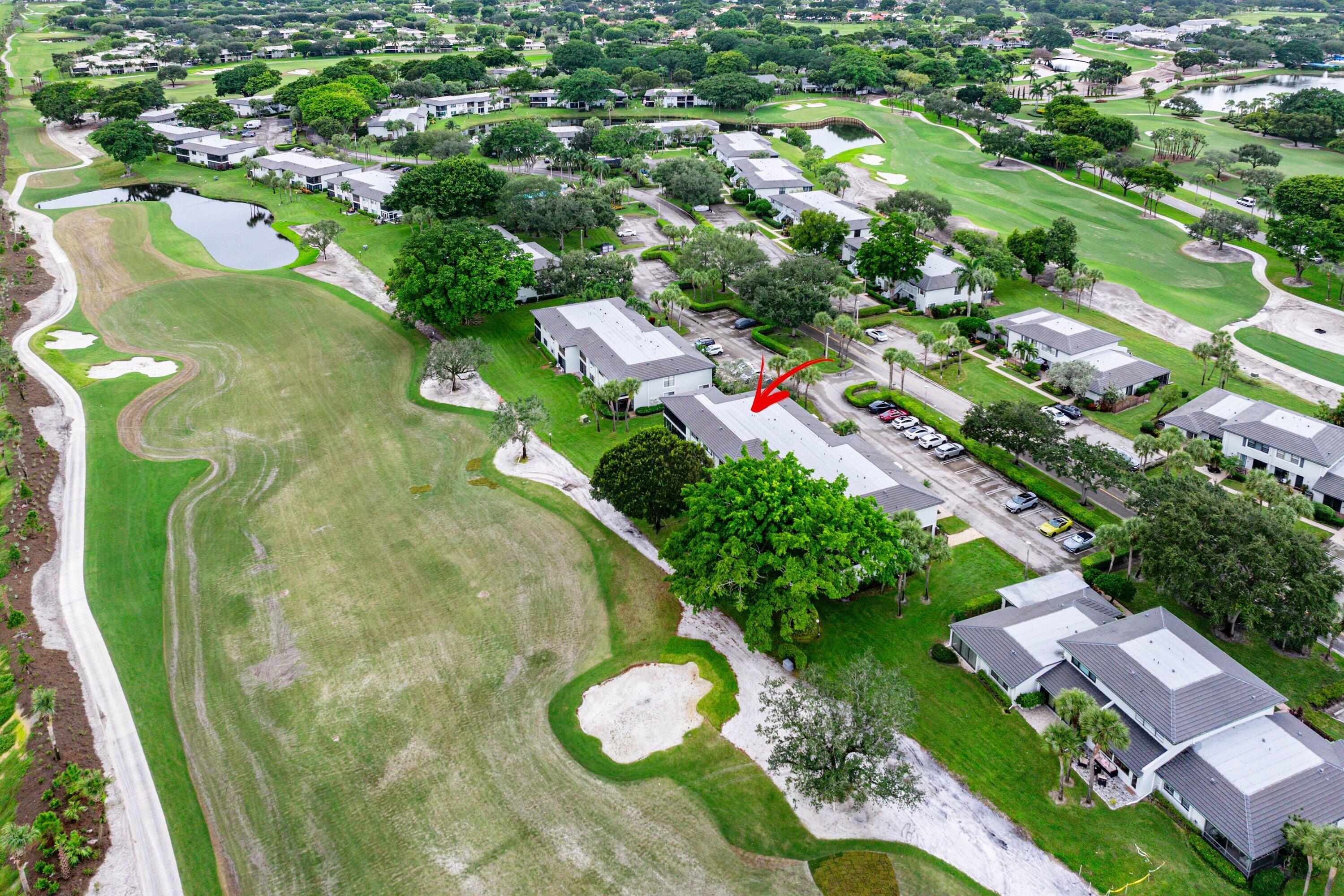 Aerial perspective featuring a multi-unit residential structure situated on a golf course with expansive fairway green space, sand bunkers, and mature landscaping