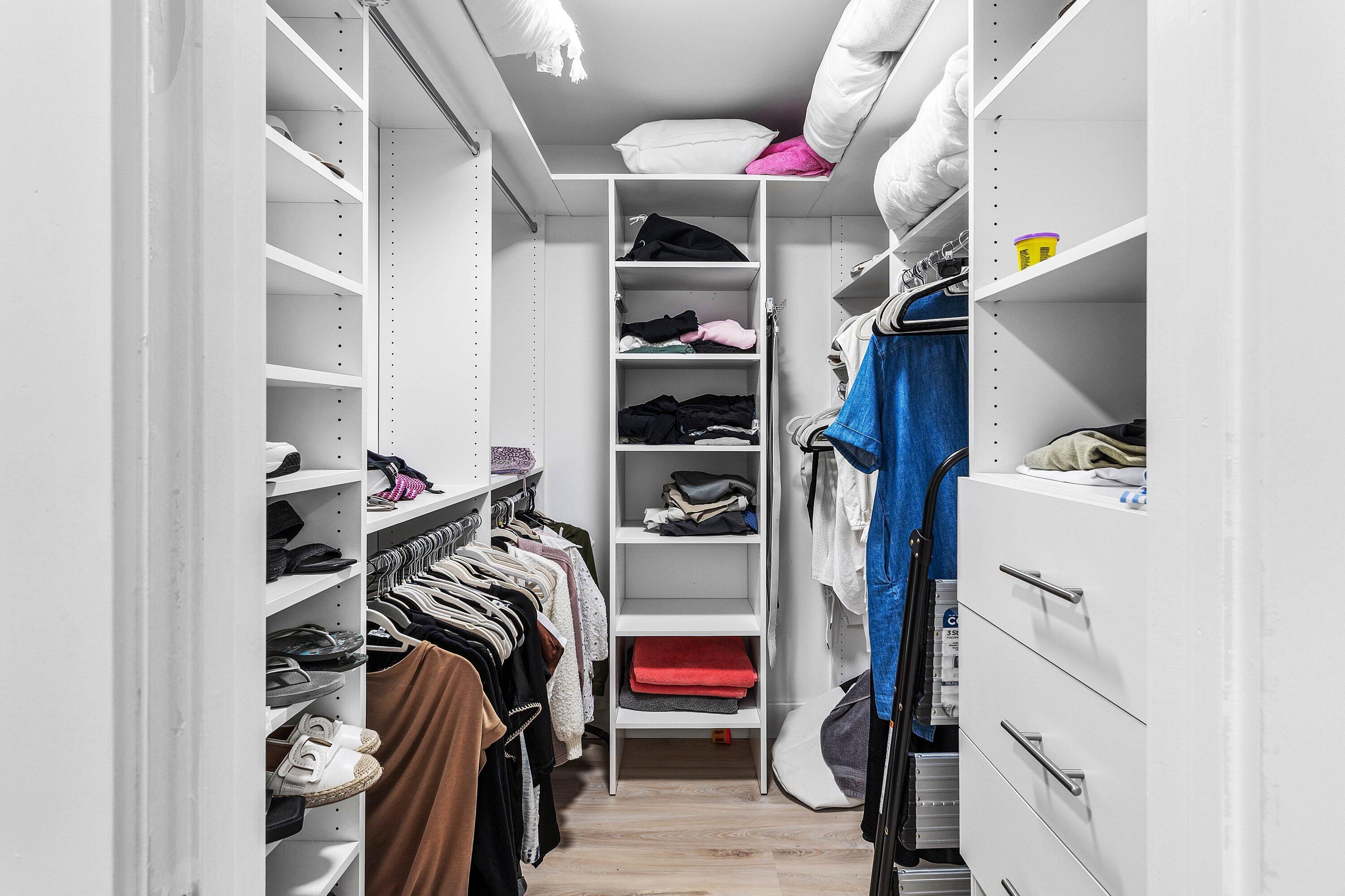 Custom walk-in closet featuring white floor-to-ceiling shelving, integrated hanging rods, built-in soft-close drawers with metallic pulls, and wood-finish flooring