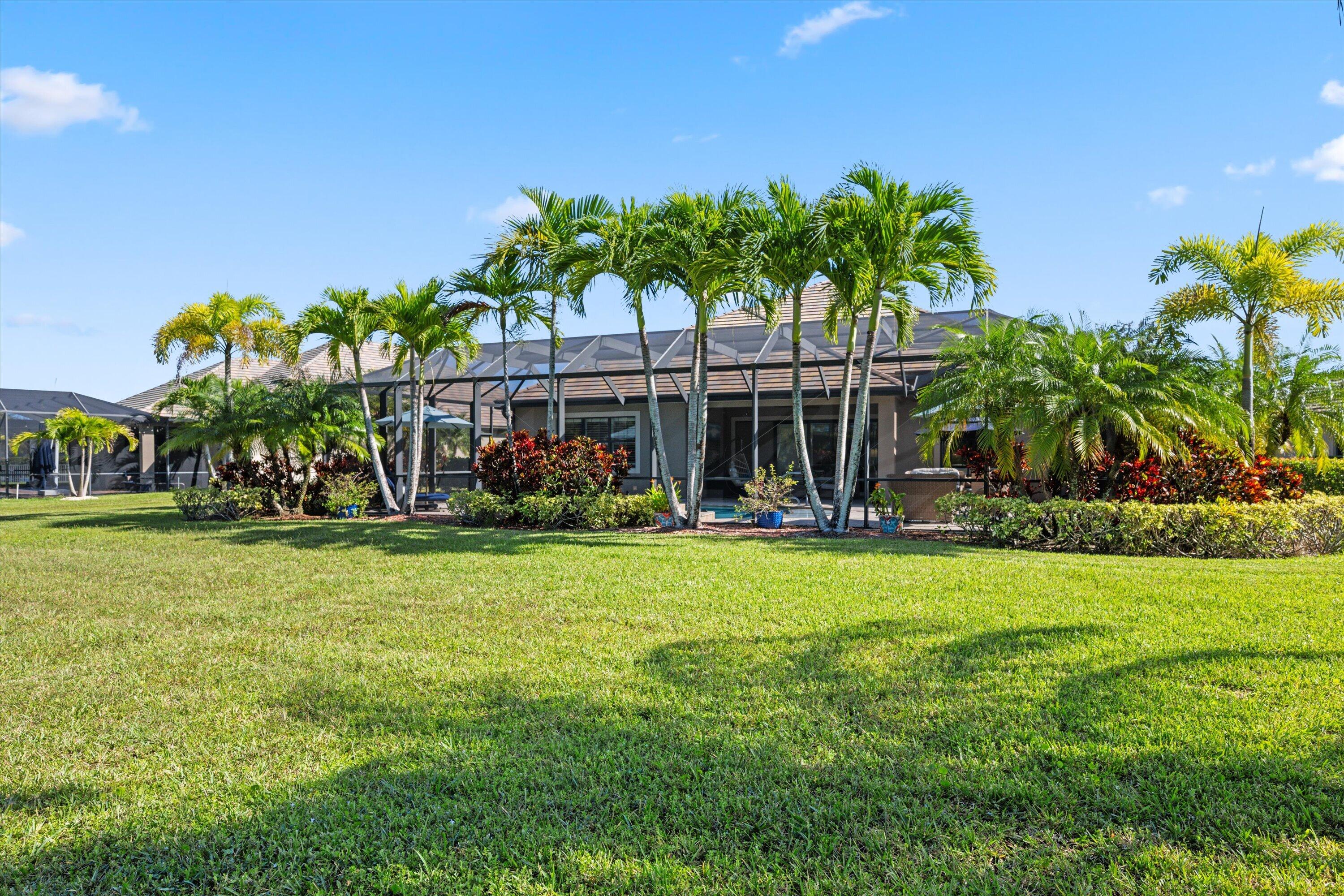 Expansive lawn featuring mature palm trees and lush landscaping, complete with a screened-in lanai