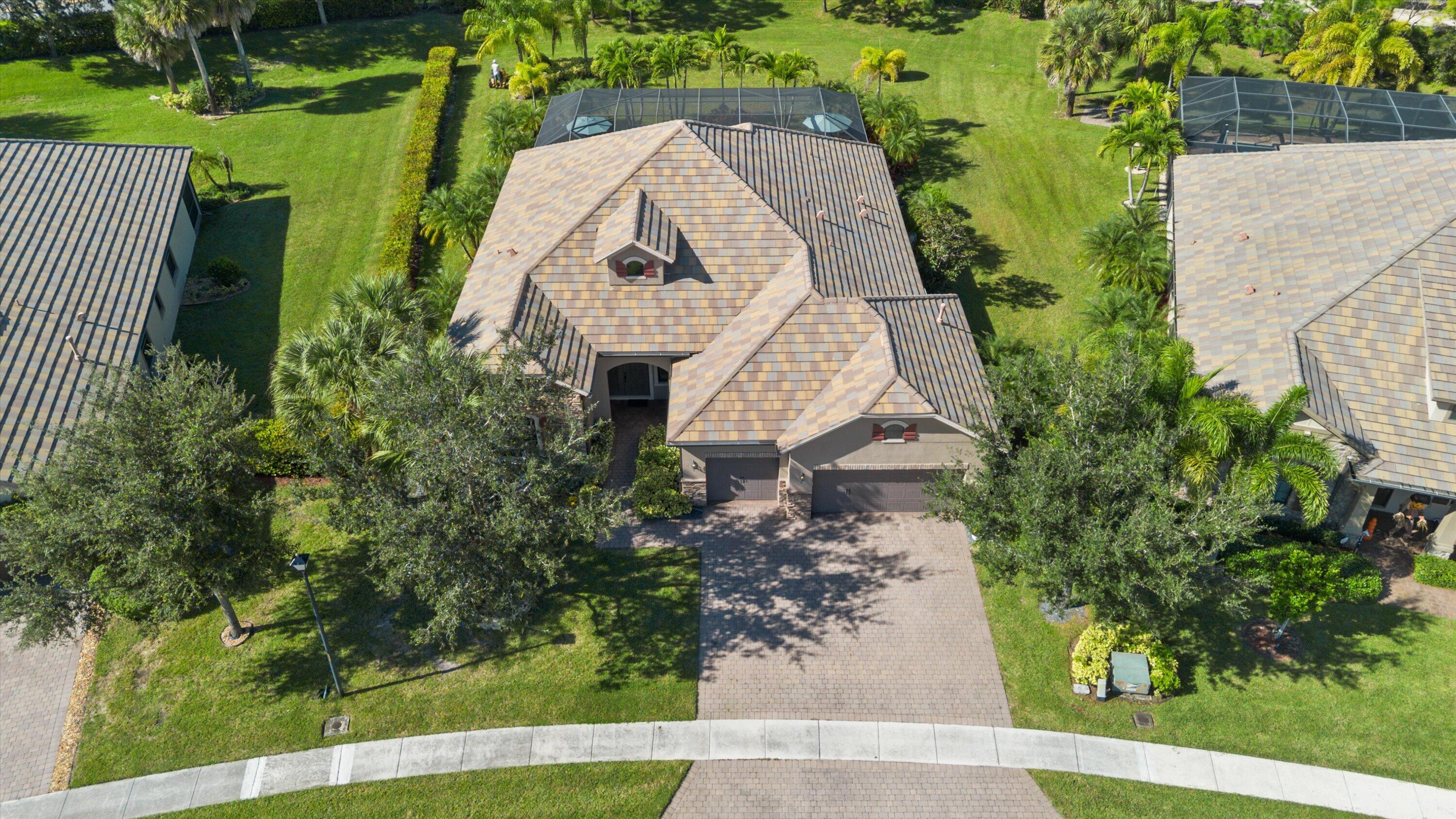 Aerial view of property featuring a screened-in lanai, a paved driveway, and mature landscaping
