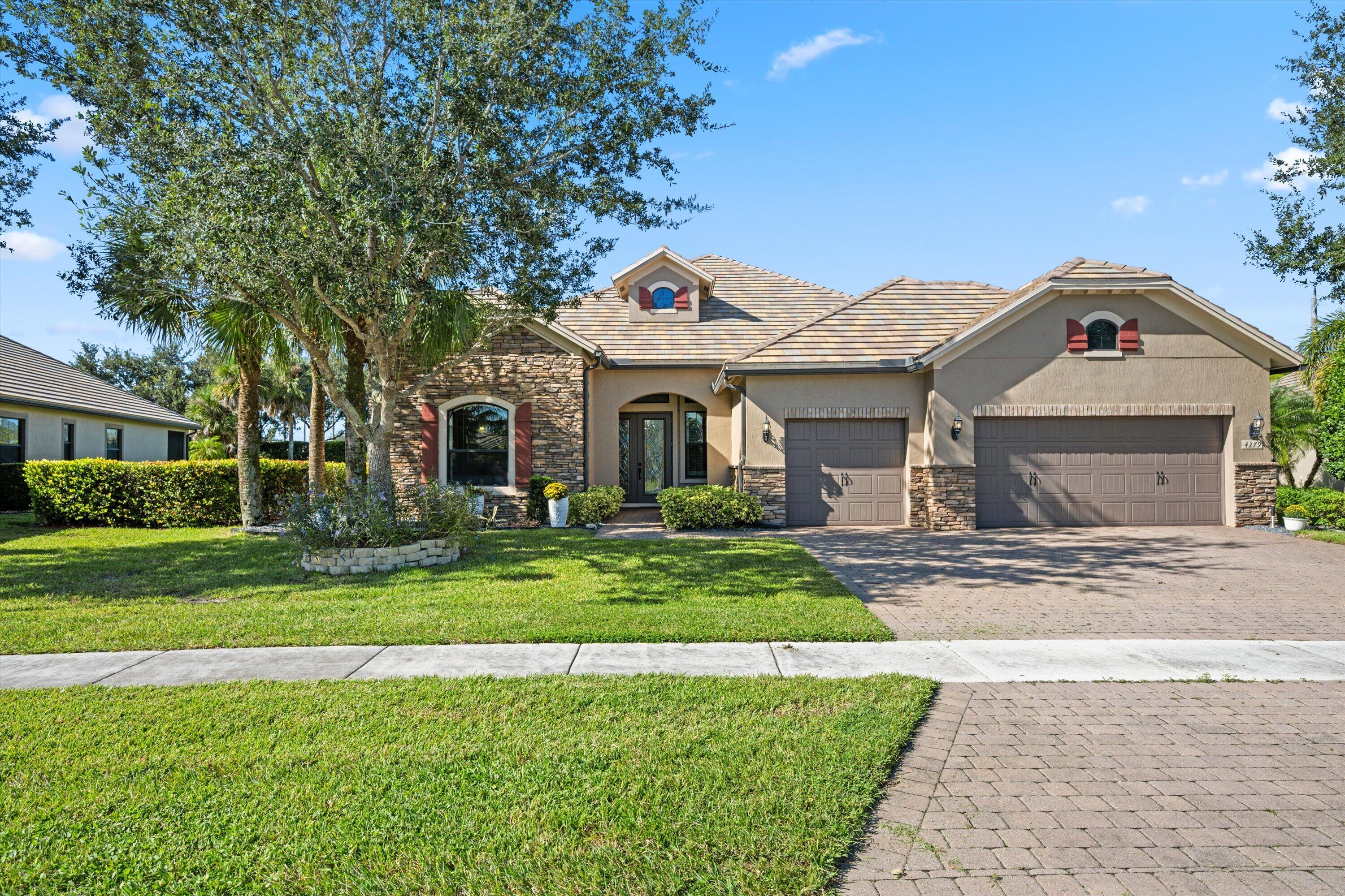 Residence featuring a stone and stucco facade, concrete tile roof, paved driveway, and arched entryway Residence featuring a stone and stucco facade, concrete tile roof, paved driveway, and arched entryway