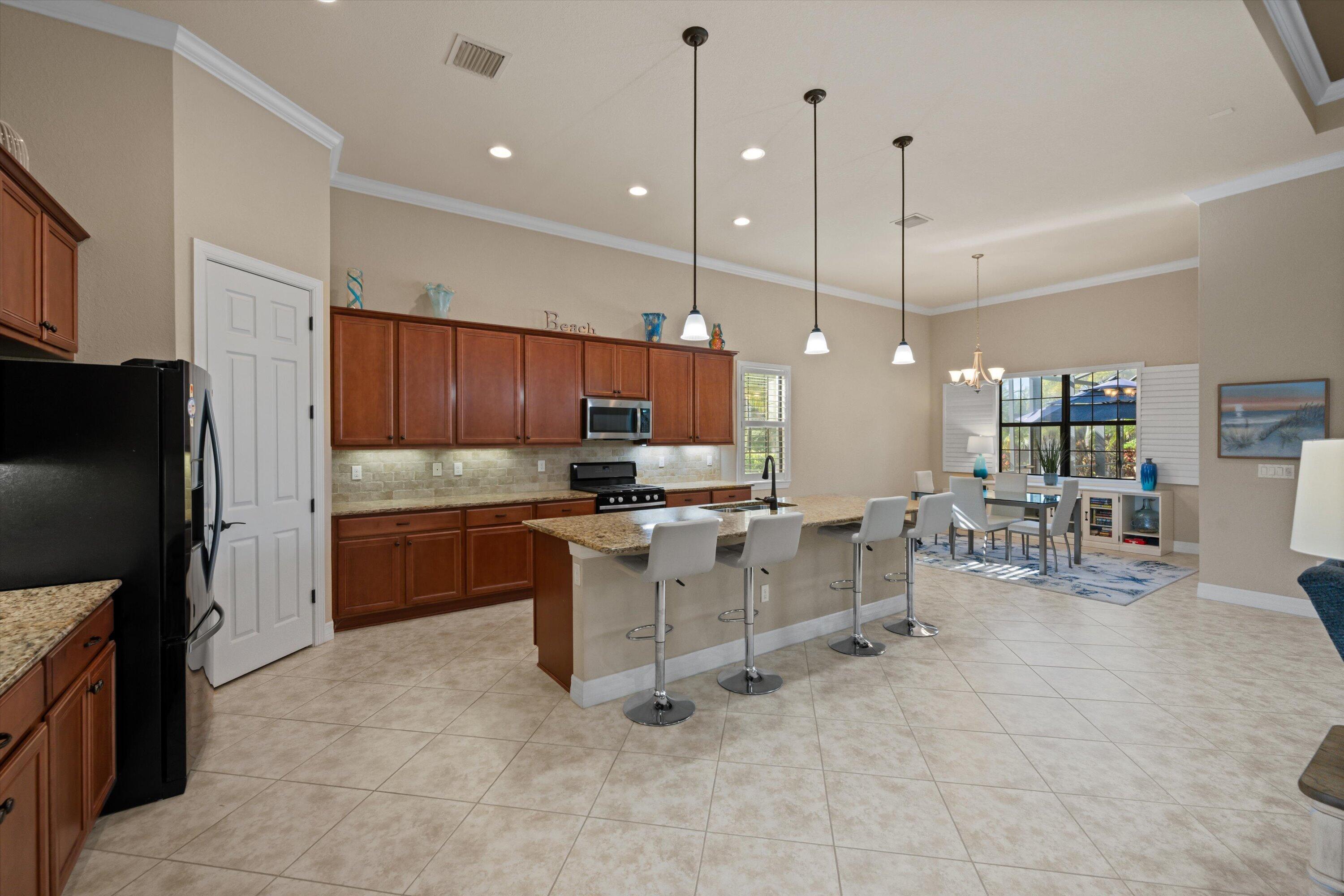 Kitchen featuring cabinetry with stained wood finish, stone-surfaced countertops, a center island with bar seating, pendant lighting, and tile flooring