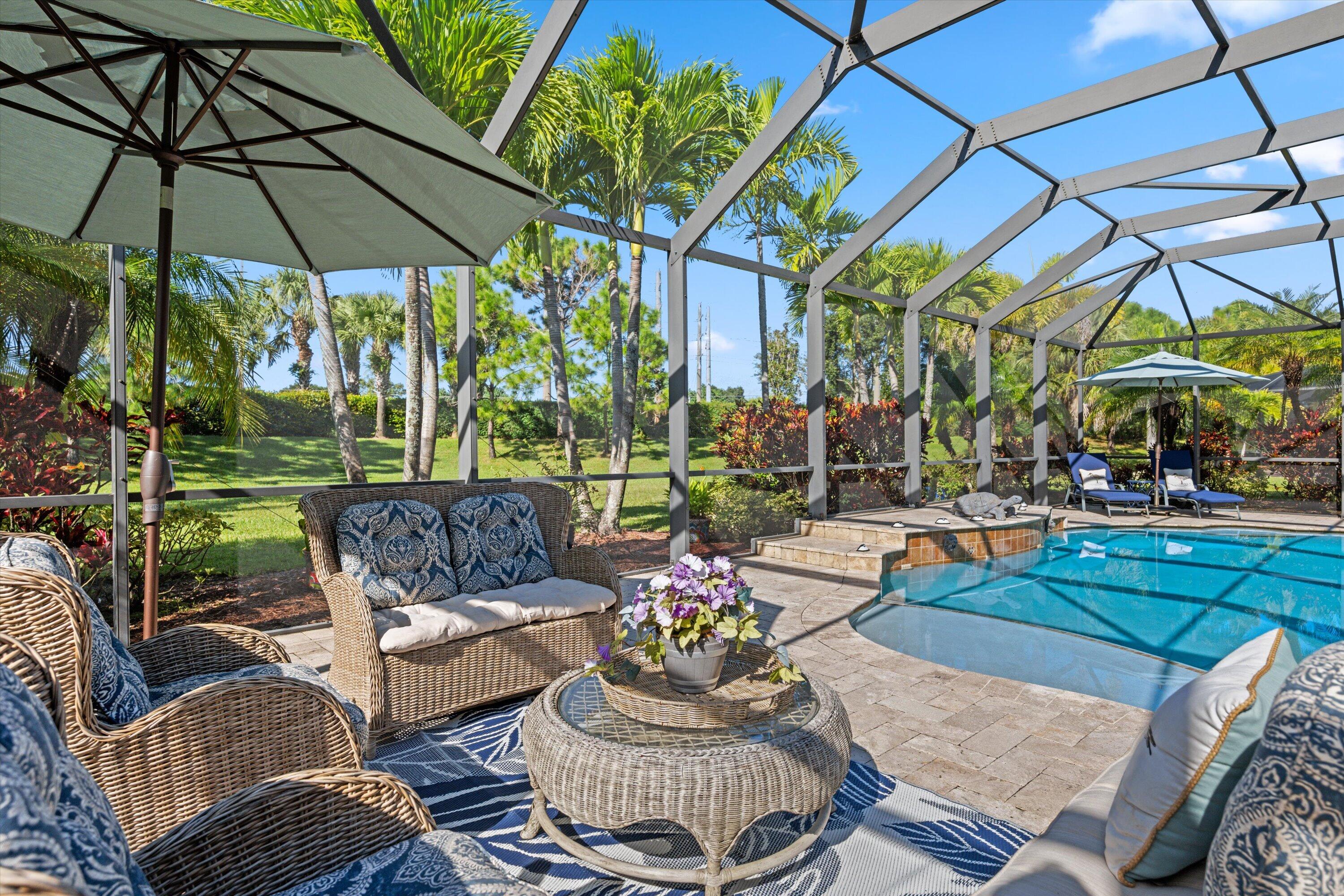 Screened-in lanai featuring a paver deck, swimming pool and surrounding mature palm trees