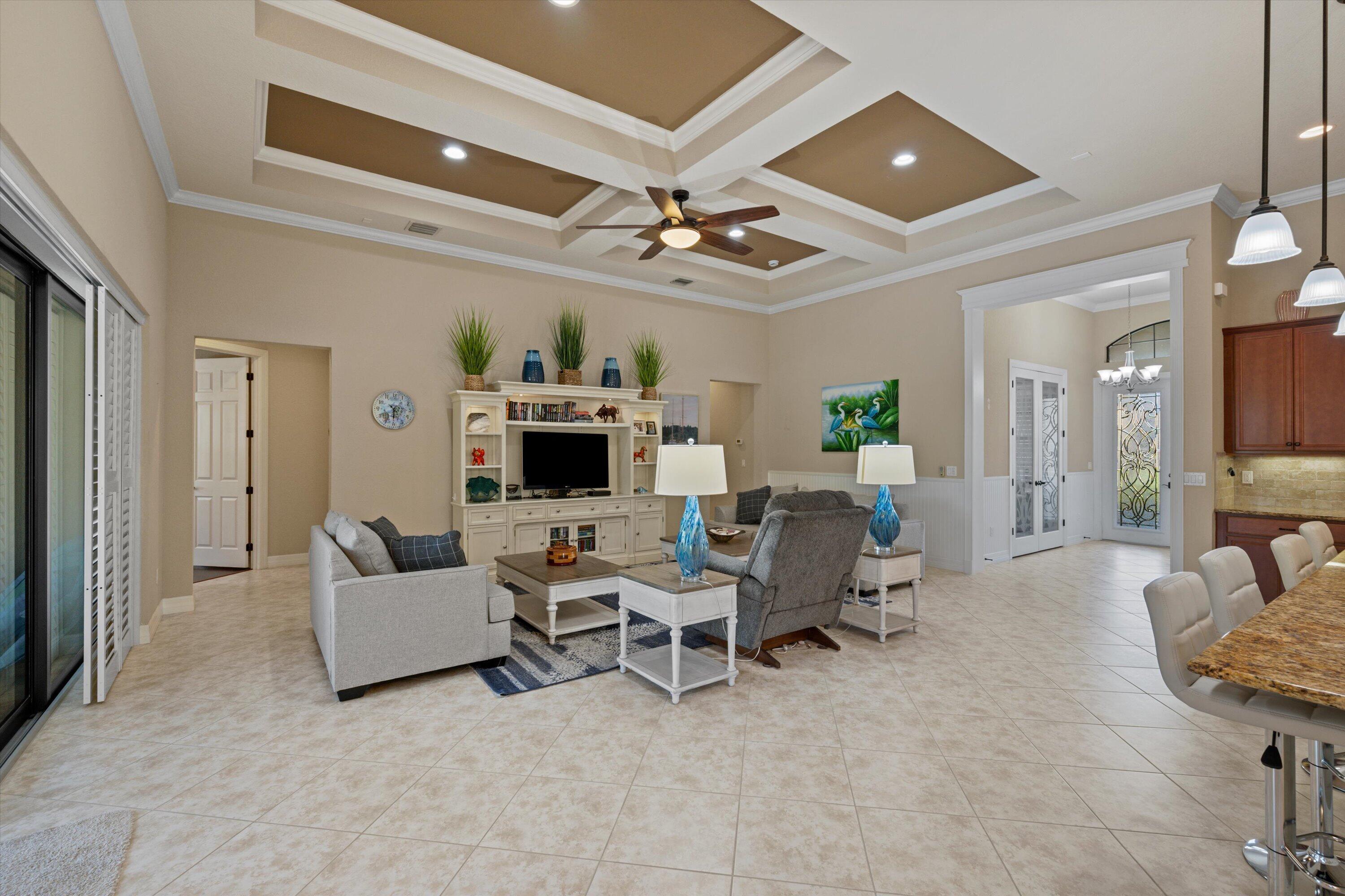 Tray ceiling with recessed lighting and a central ceiling fan, built-in media cabinetry, tile flooring, stone-surfaced kitchen island, and pendant light fixtures