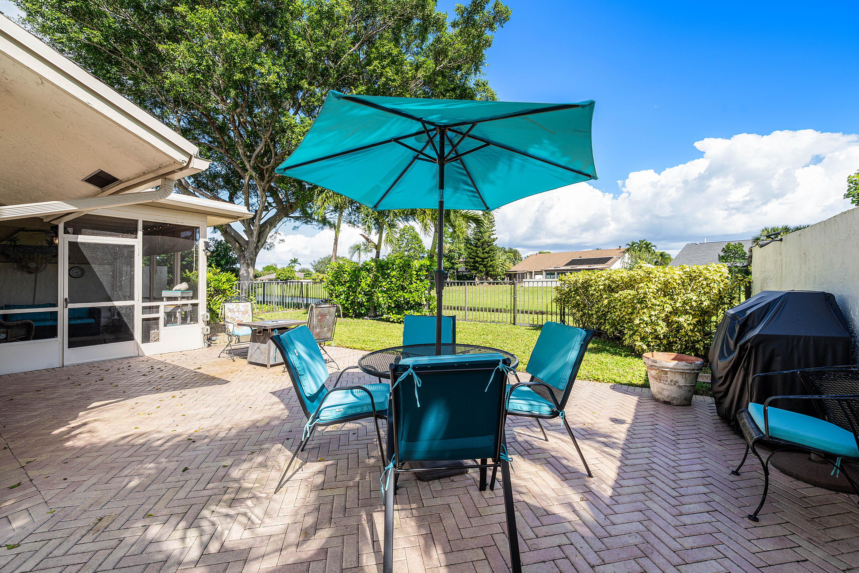 Brick paver patio featuring an enclosed screened-in porch, metal perimeter fencing, and mature landscaping