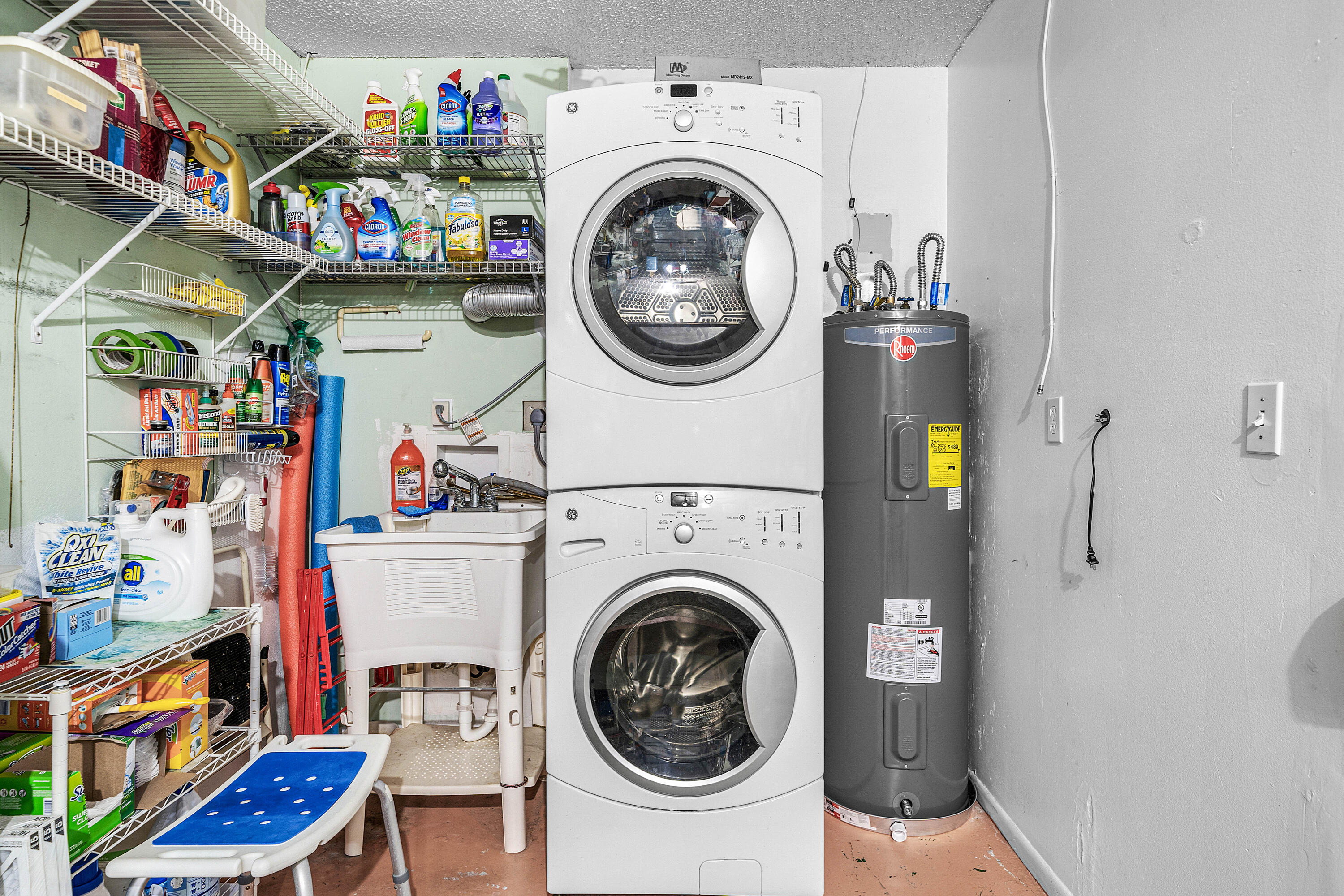 Laundry utility area featuring a stacked GE washer and dryer unit, a white basin utility sink, and installed metal wire shelving