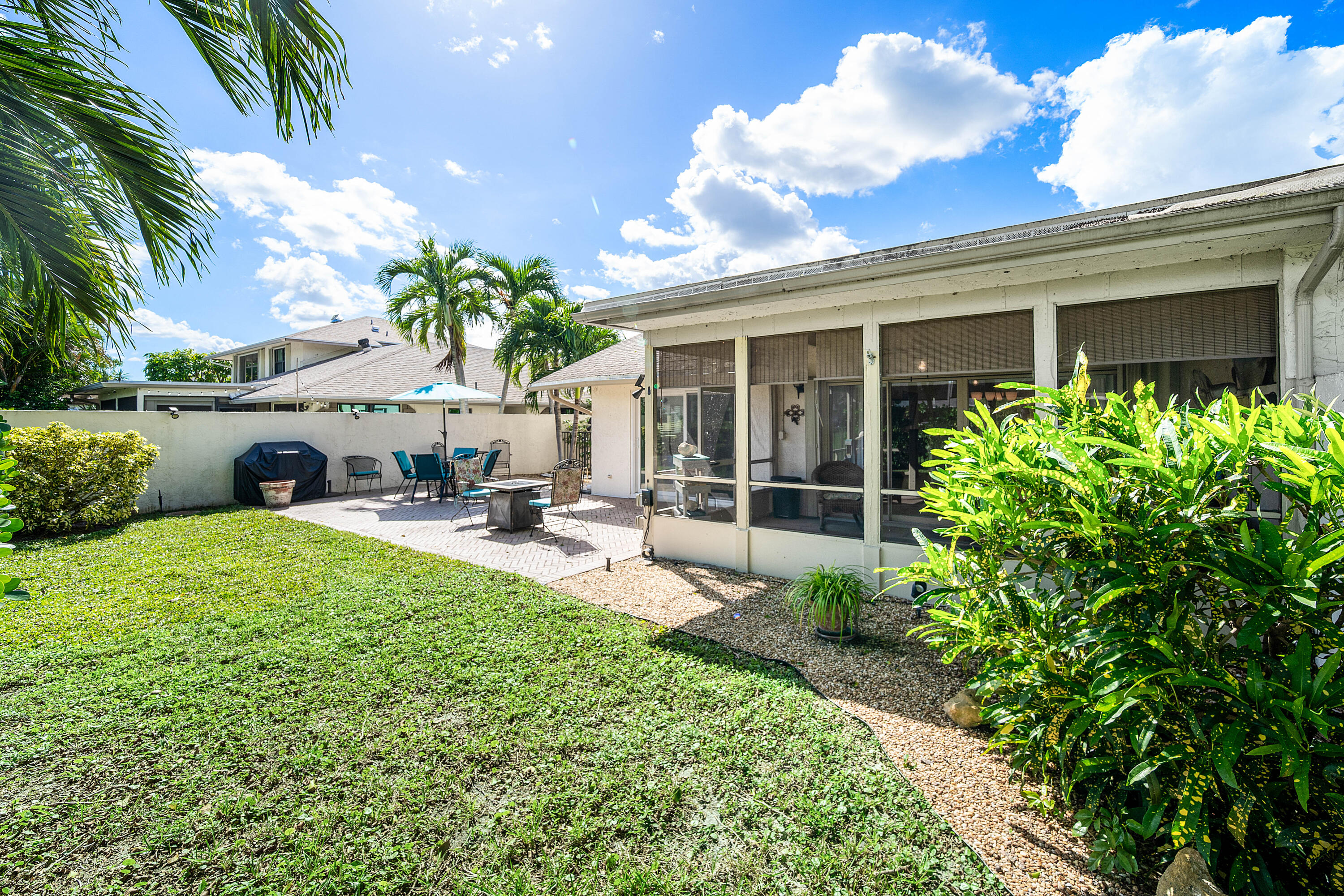 Backyard featuring a screened-in lanai, concrete paver patio, stone ground cover, and perimeter privacy wall