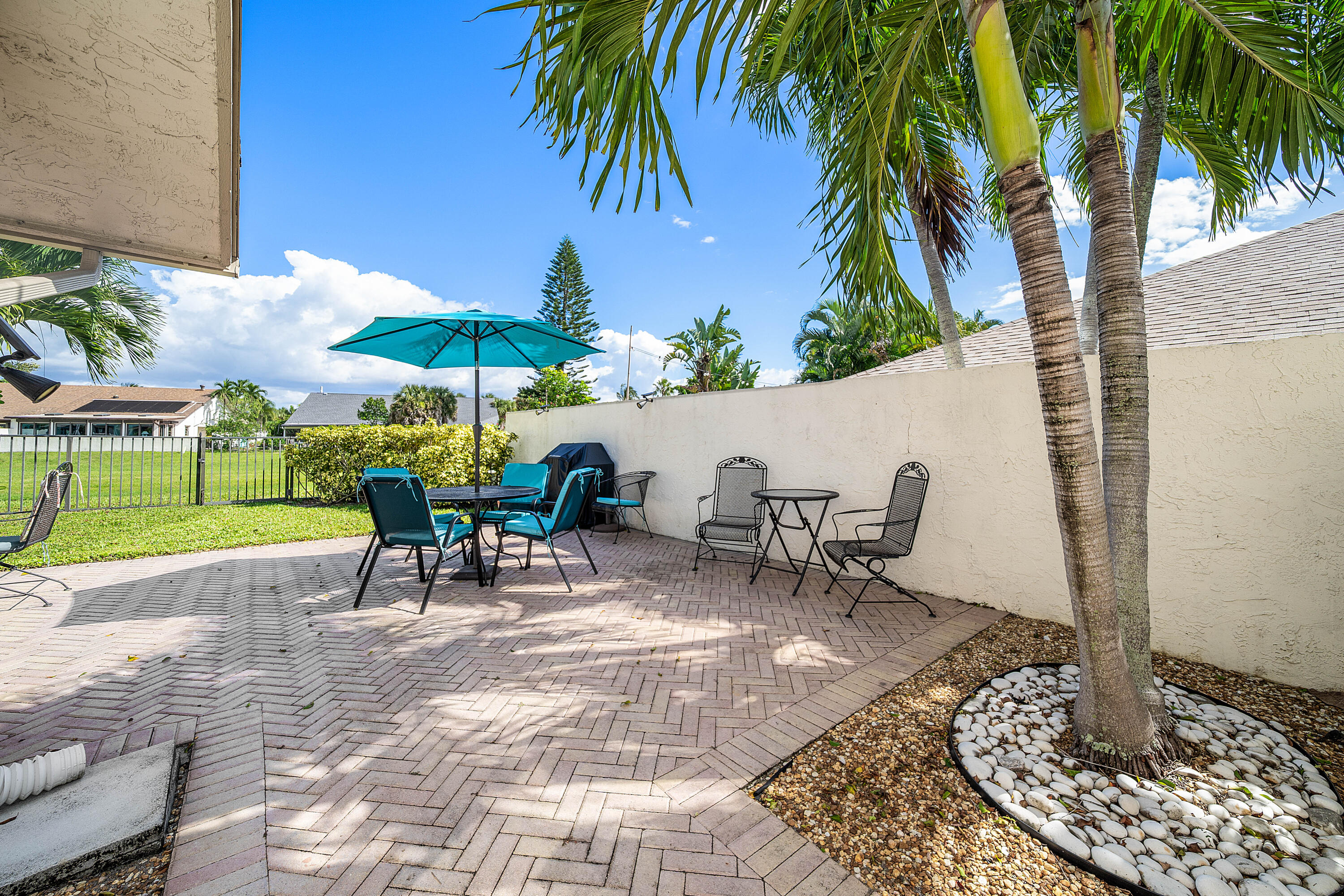 Outdoor patio featuring herringbone-patterned brick pavers, a privacy wall, mature palm trees, and decorative stone landscaping