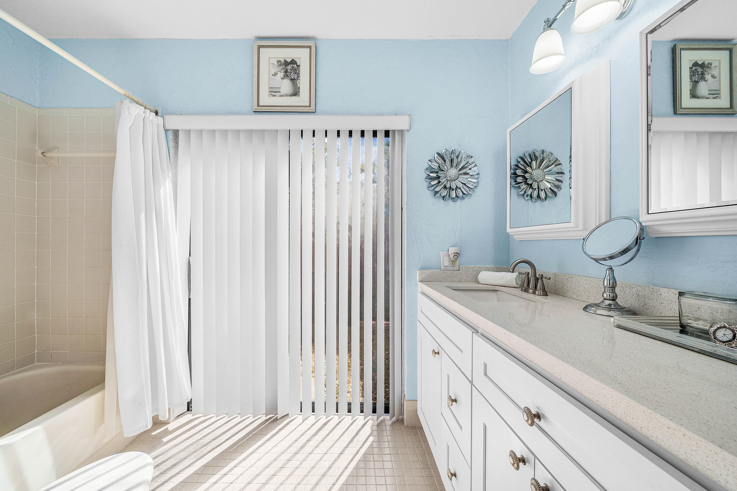 Bathroom featuring a double-sink vanity with stone-composite countertop, white cabinetry, integrated medicine cabinets, and sliding glass patio doors with vertical blinds