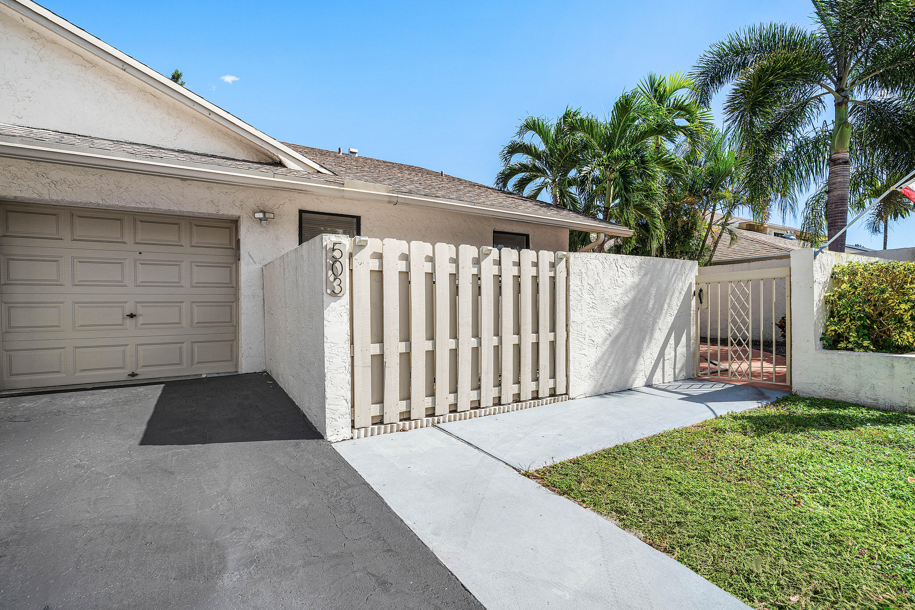 Stucco exterior featuring an attached one-car garage, private enclosed courtyard with vertical slat fencing, paved walkway, and manicured lawn