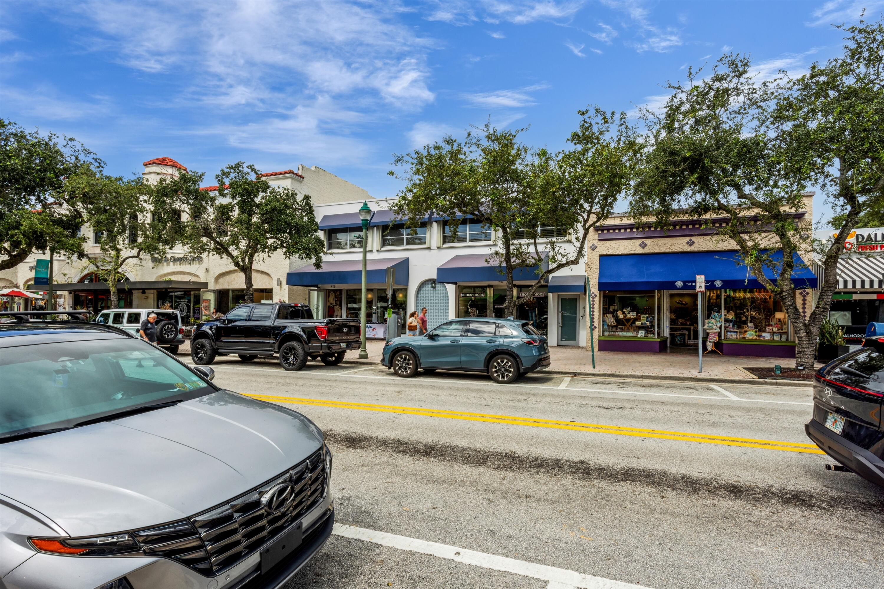 Commercial storefronts featuring arched entryway detailing, blue fabric awnings, expansive glass display windows, and masonry exterior finishes