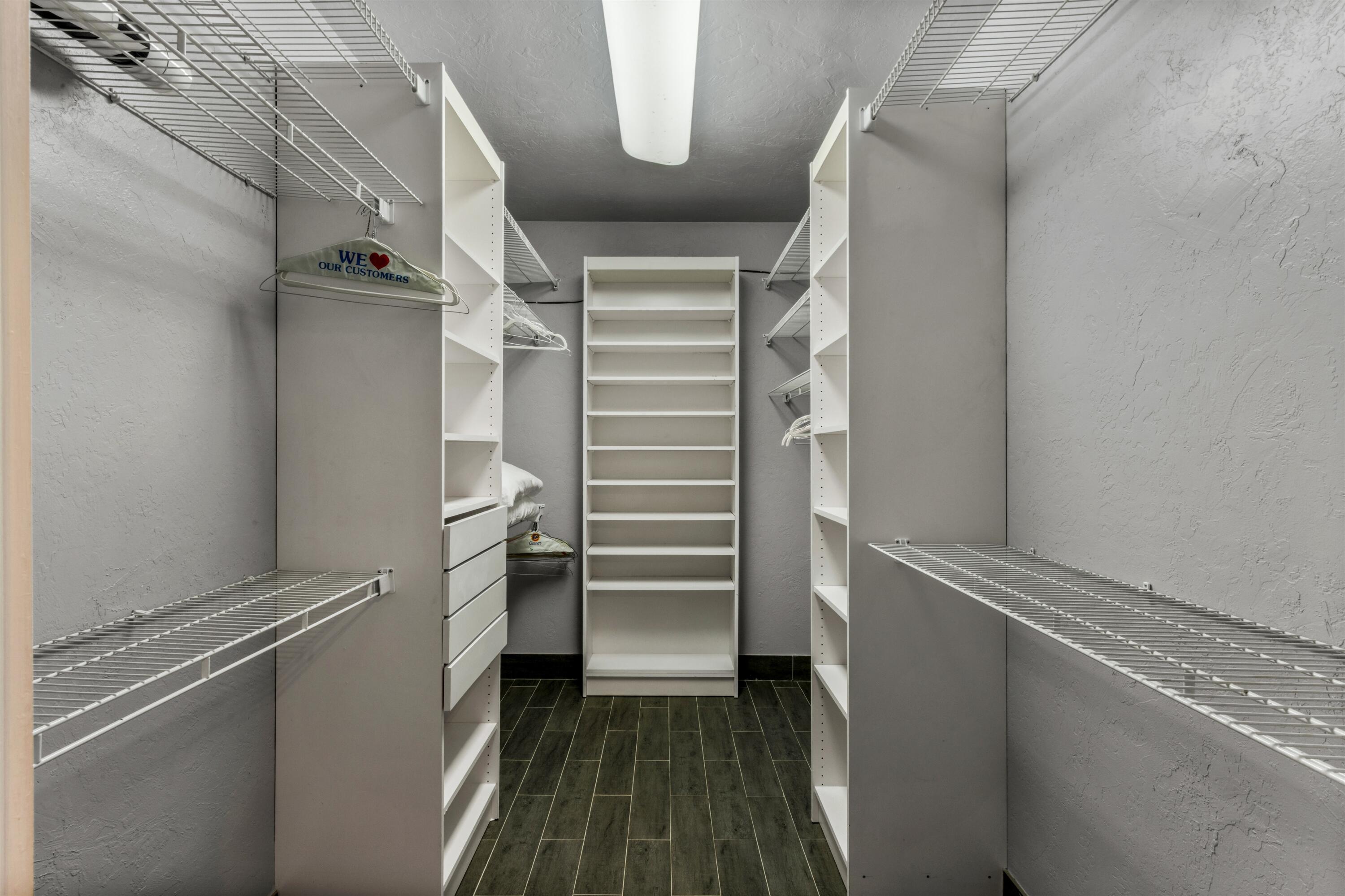 Walk-in closet featuring white built-in shelving, integrated storage drawers, wire shelving racks, and wood-finish tile flooring