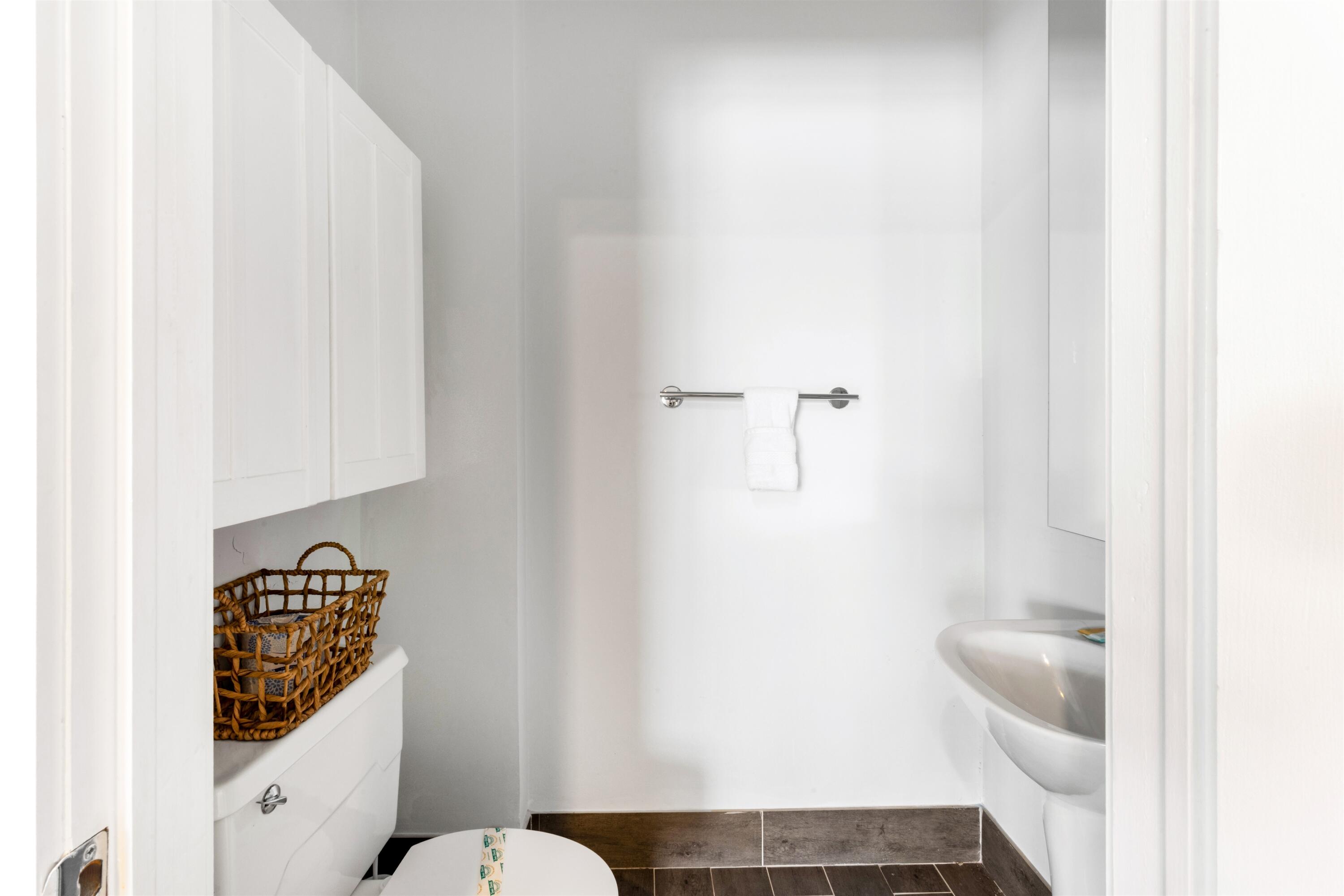Wall-mounted white cabinetry, white pedestal sink, polished chrome faucet hardware, wall-mounted towel bar, and dark-toned floor tiling
