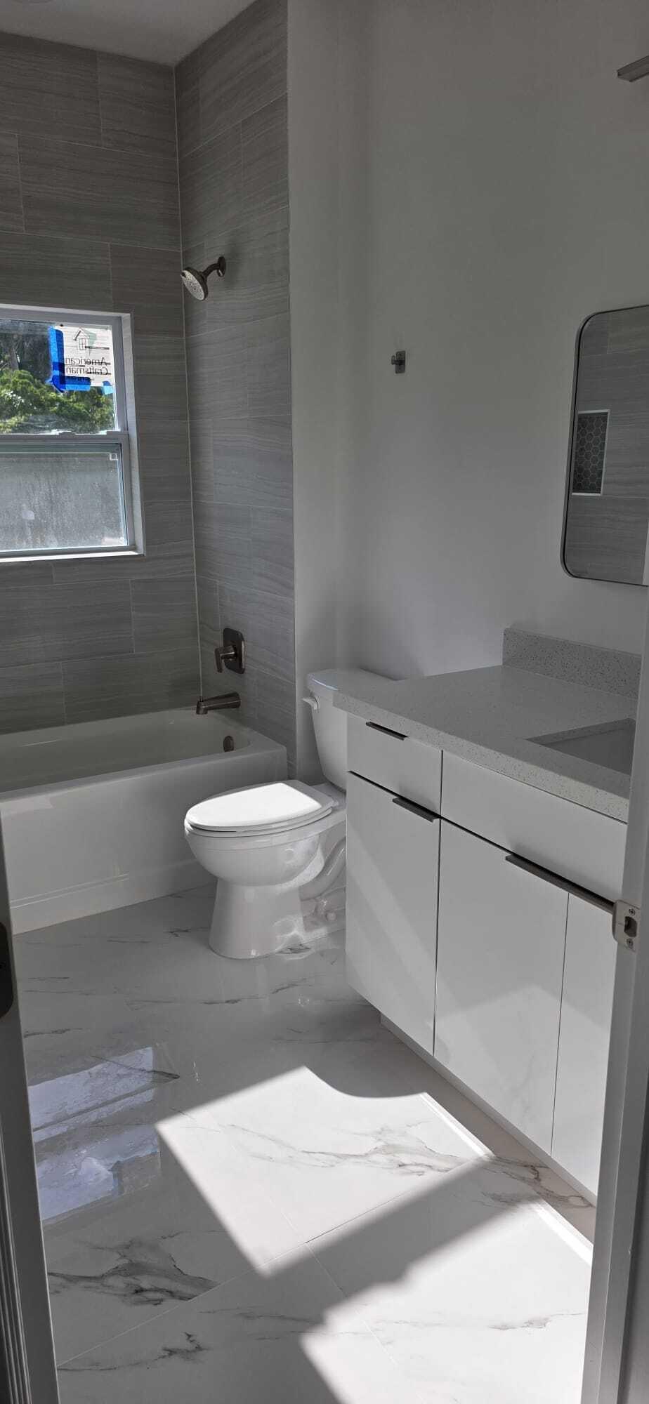 Bathroom featuring large-format marble-finish flooring, a white vanity with a composite countertop, polished chrome fixtures, and a tub enclosure with full-height horizontal wall tile