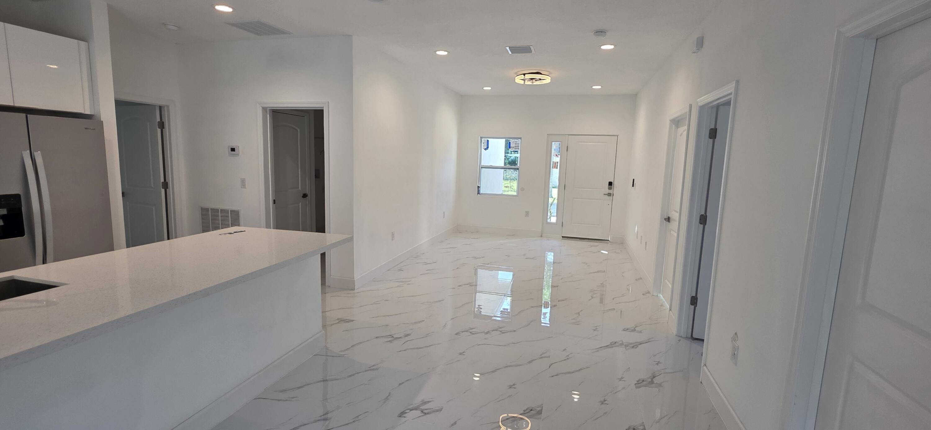 Open-concept interior featuring large-format tile flooring with marble-style veining, recessed lighting, and a kitchen island with stone-surface countertops