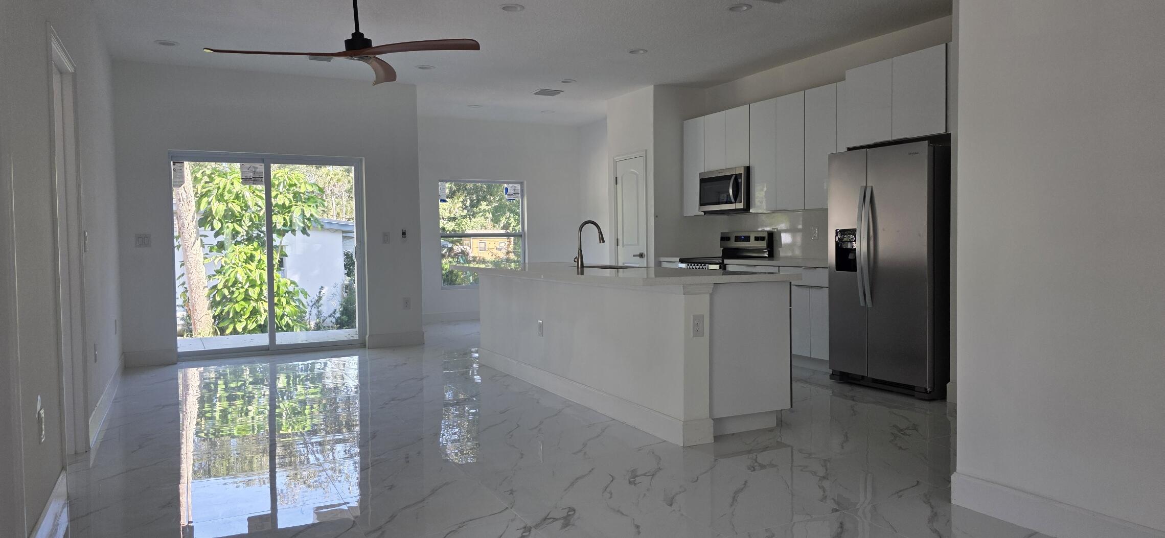 Kitchen featuring white cabinetry, an island with a stone-surface countertop, stainless steel appliances, polished stone-finish flooring, and a ceiling fan