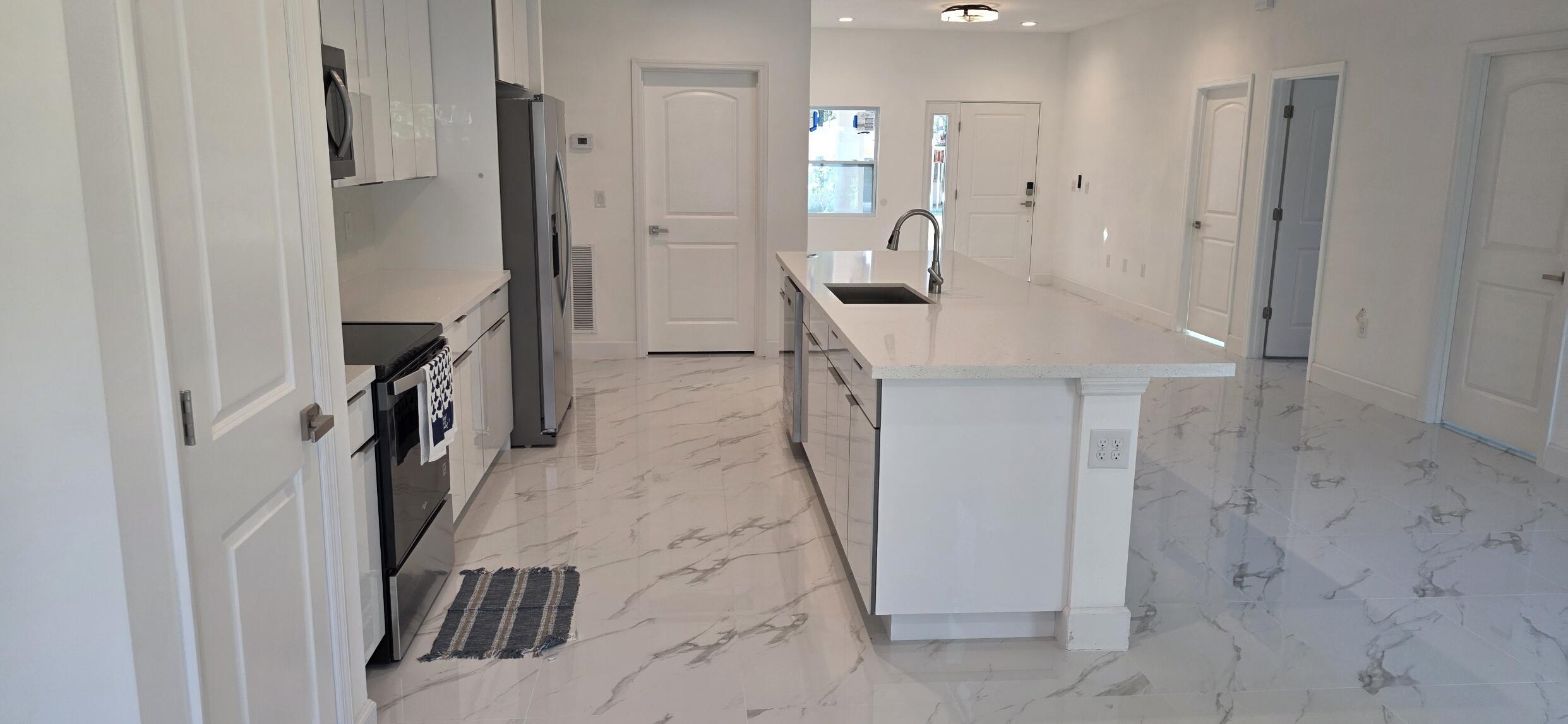 Kitchen featuring high-gloss white cabinetry, a center island with a stone-finish countertop, stainless steel appliances, and large-format tile flooring with a marble-finish pattern
