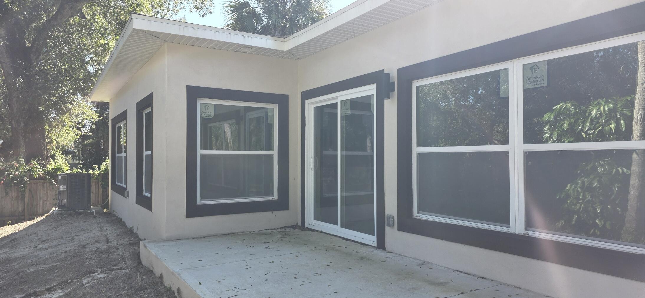 Stucco exterior featuring dark-trimmed windows, sliding glass door, and a concrete patio