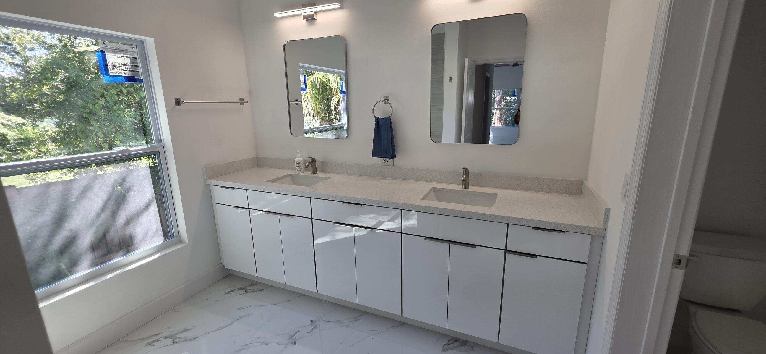 Dual-vanity cabinet with sleek white finish, expansive stone-surface countertop, dual rectangular undermount sinks, frameless wall mirrors, and high-gloss tile flooring