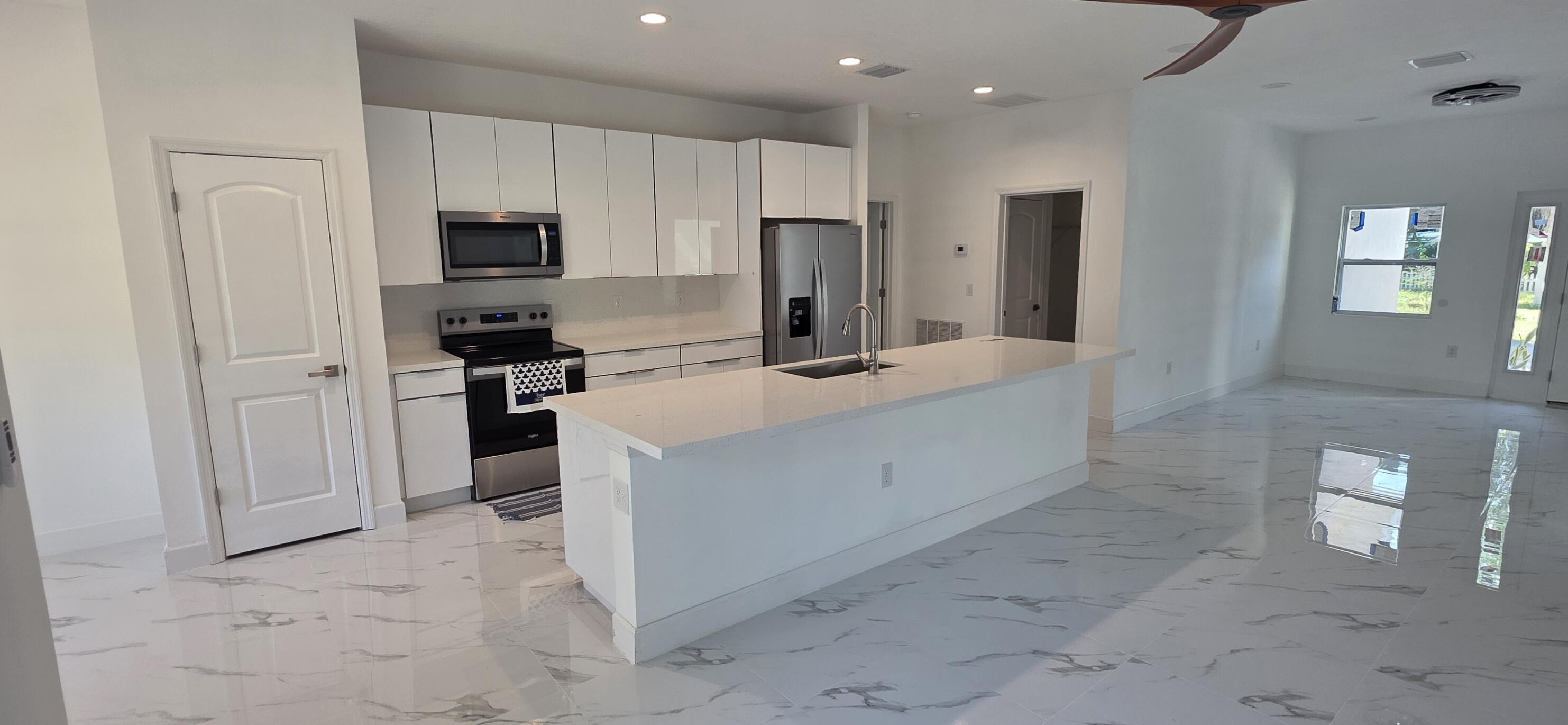 Kitchen featuring white flat-panel cabinetry, quartz countertops, a central island with an integrated sink, stainless steel appliances, and large-format tile flooring
