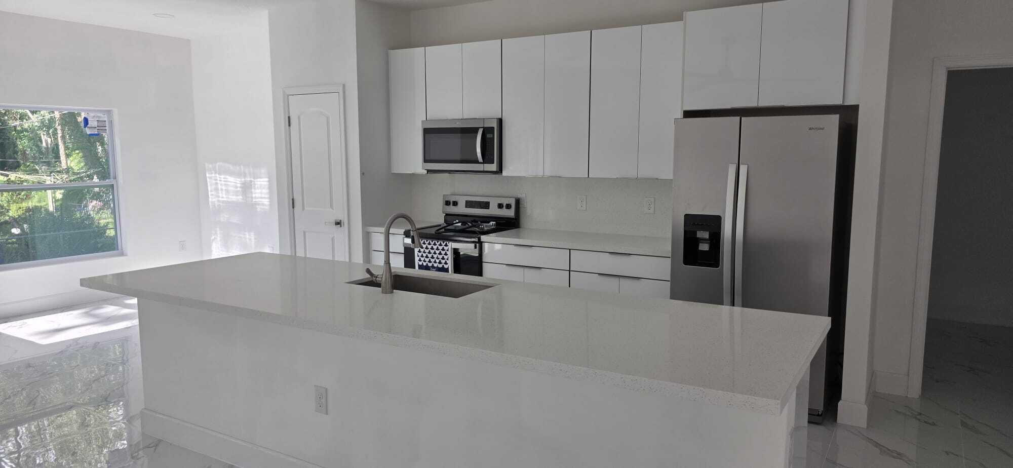 Kitchen featuring a central island with a quartz countertop, white flat-panel cabinetry, stainless steel appliances, and tile flooring
